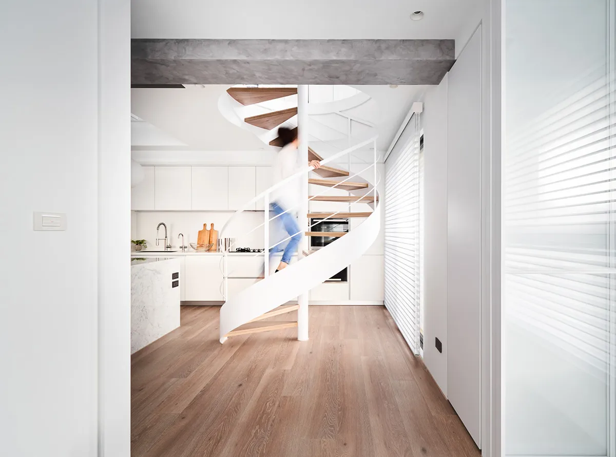 A modern kitchen with wooden flooring, metal railings, and marble countertops, featuring a spiral staircase.