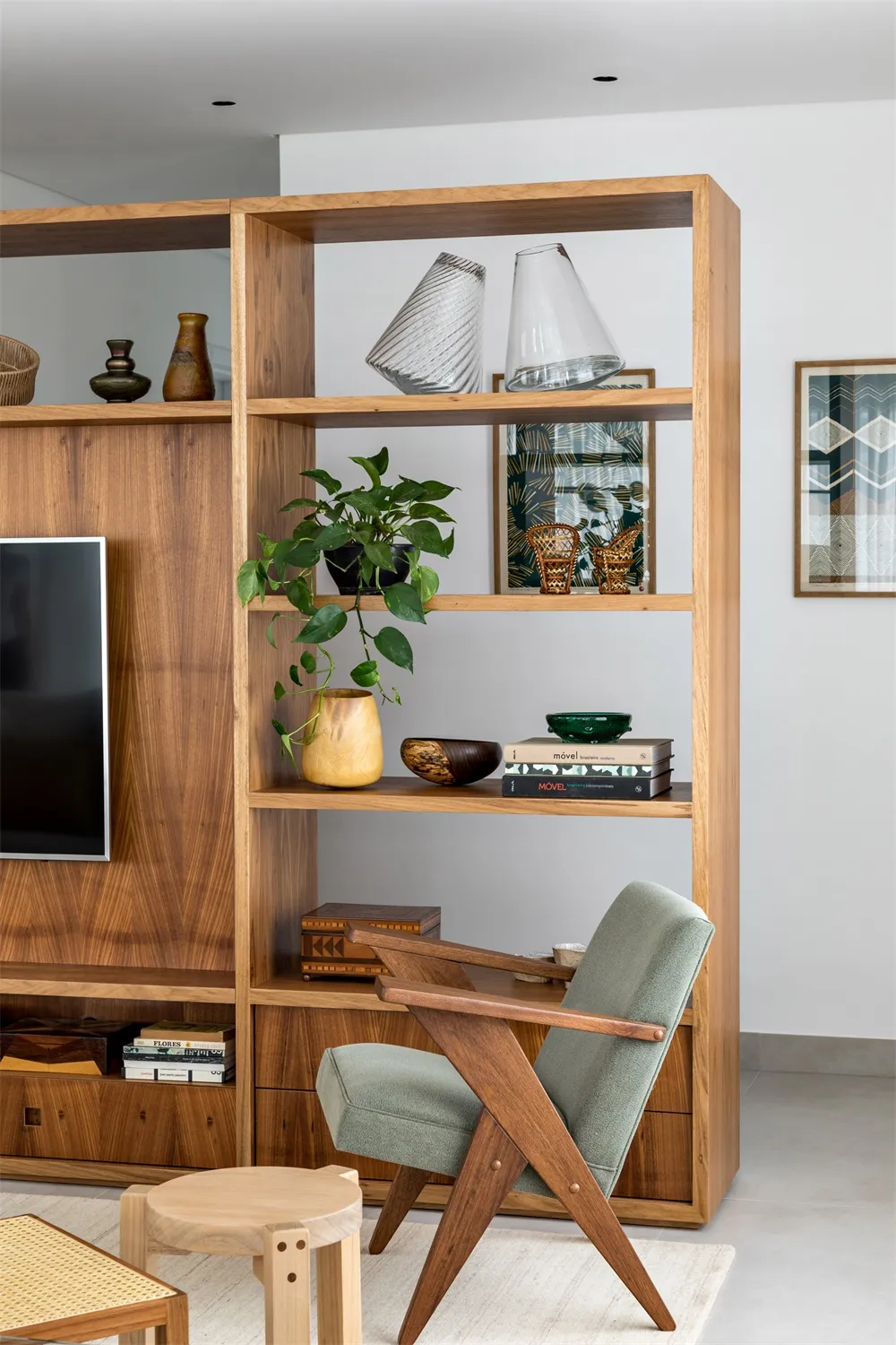 A modern living room featuring a wooden shelving unit with a green plant, decorative items, and a television.