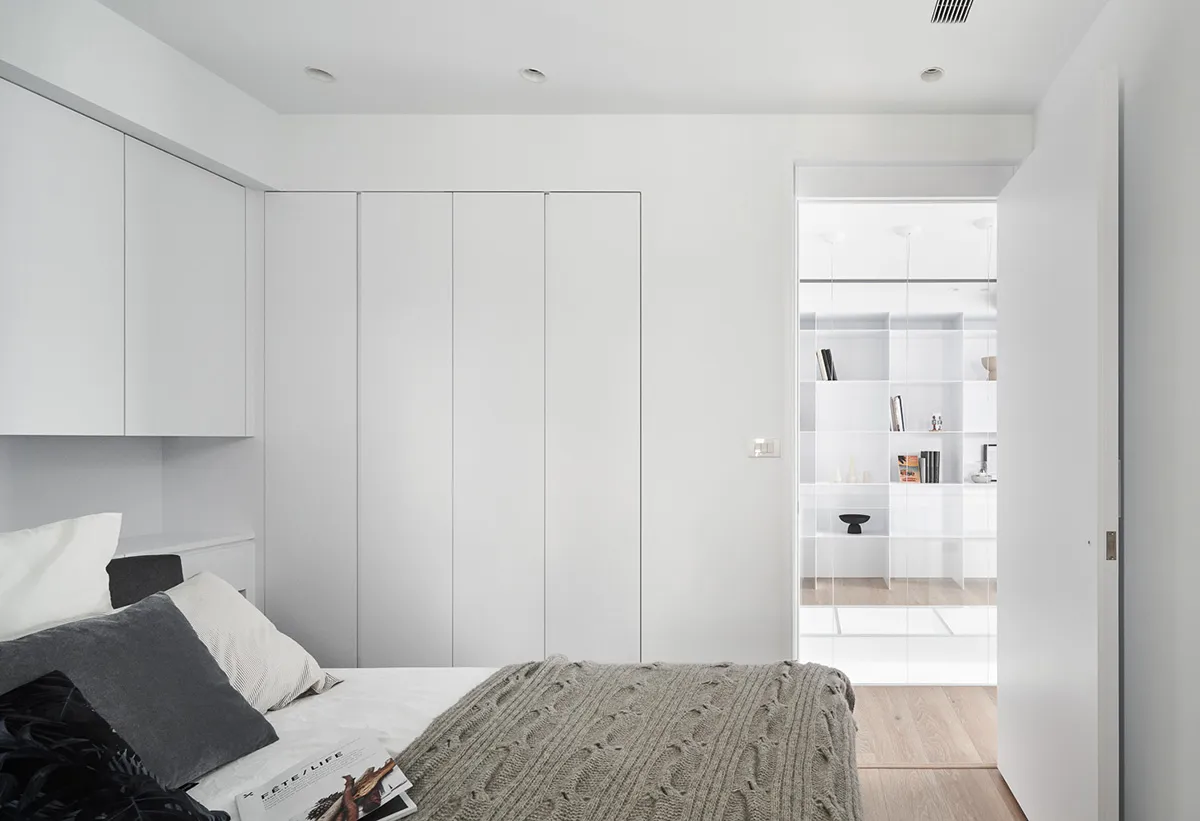 A modern minimalist bedroom featuring white cabinets and wooden floor with a comfortable bed.