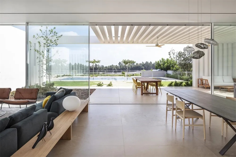 A modern minimalist living room with concrete flooring, a large glass wall, and a sleek, contemporary sofa.