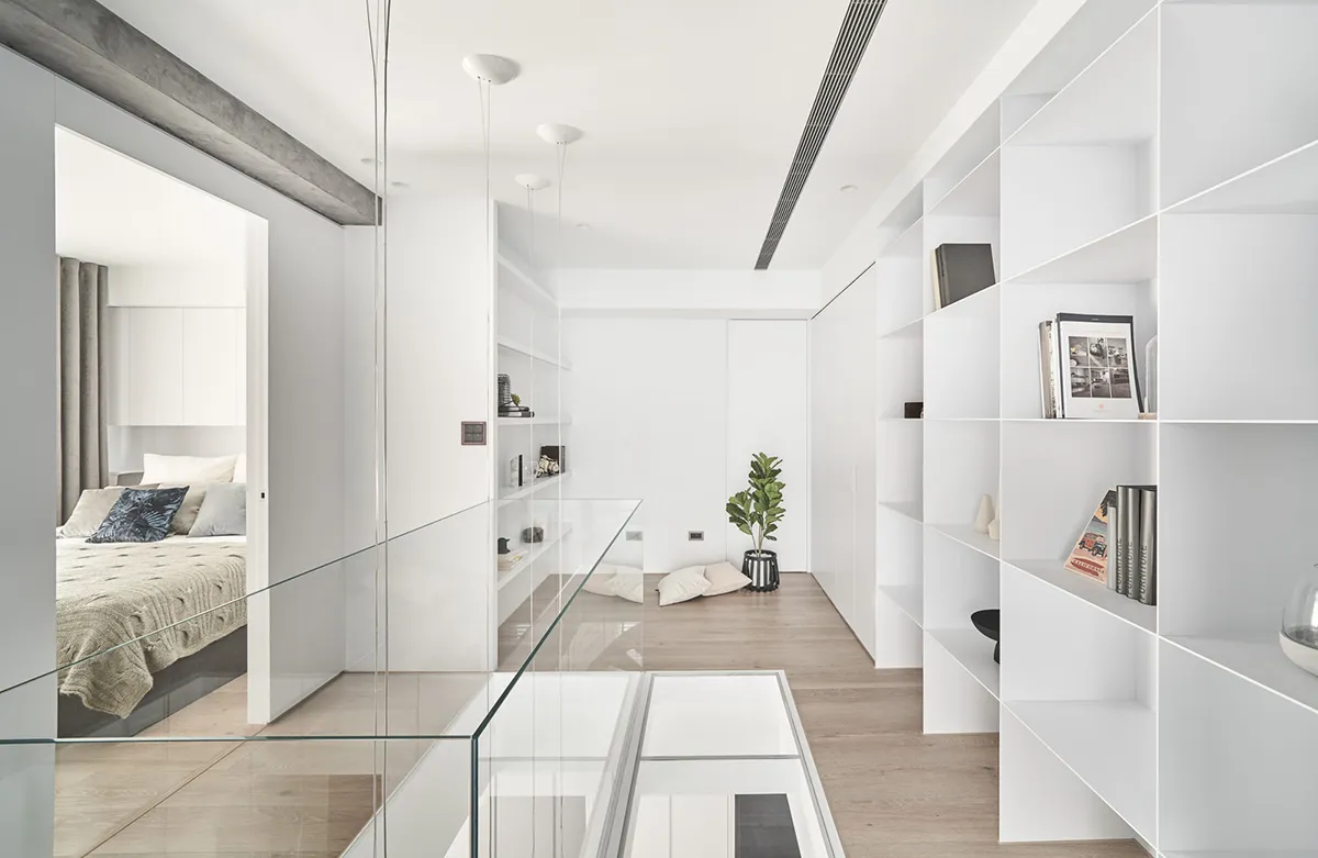 A minimalist living room with white walls, wooden flooring, and a glass railing.