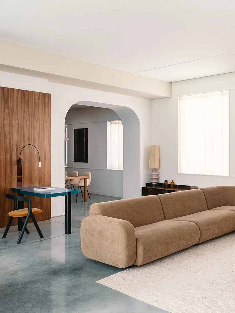 Modern minimalist living room featuring a beige fabric sofa on a cream rug, with a geometric light fixture and a dining area