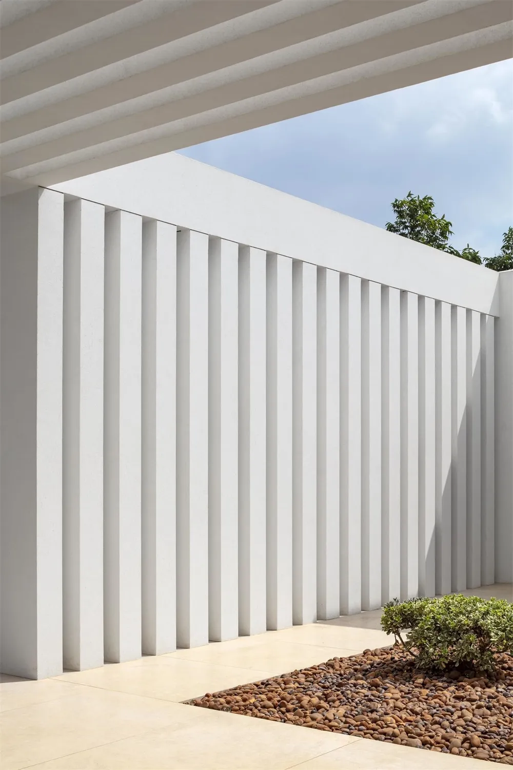 A minimalist concrete wall with vertical slats under a covered patio area.