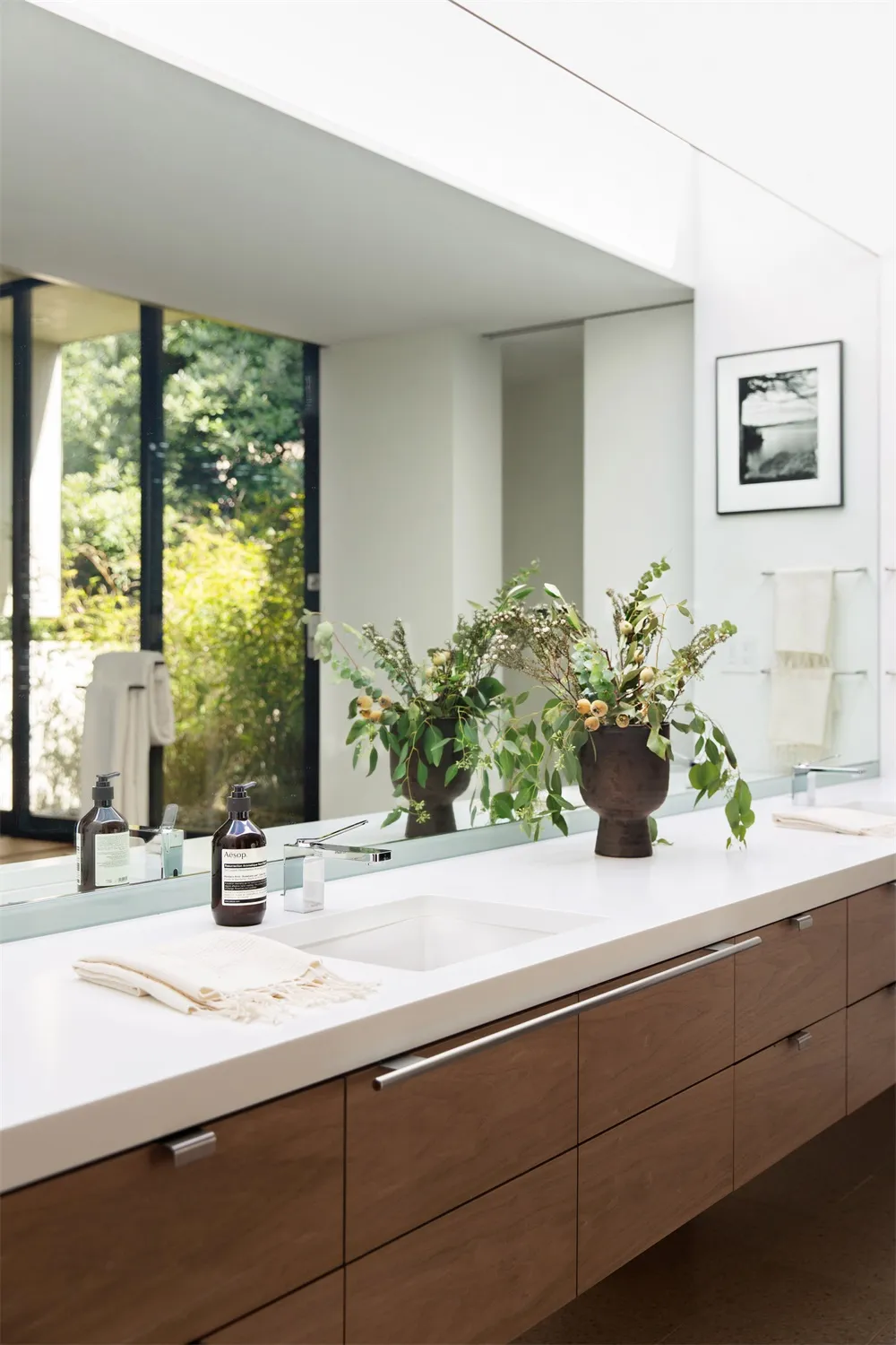 The image features a modern bathroom with natural wood cabinetry and marble countertops, adorned with greenery and elegant de