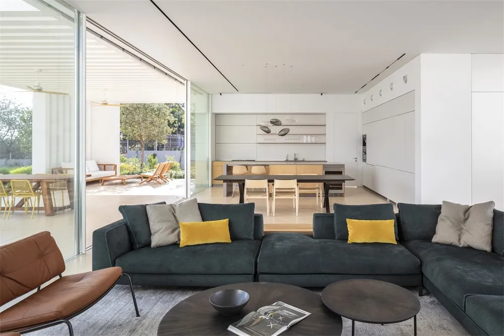 A modern living room featuring a dark green sectional sofa adorned with mustard yellow accent pillows, set against a minimali