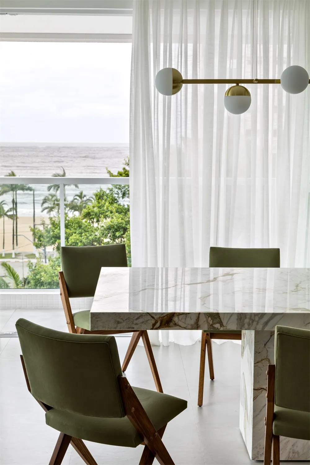 Modern dining room with marble table and green chairs, overlooking the ocean.