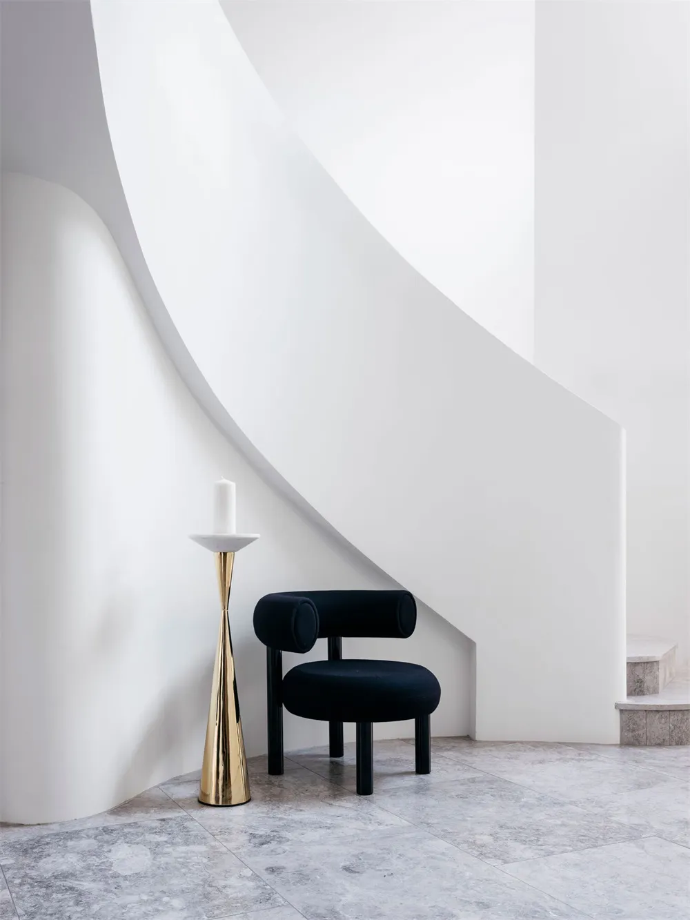 A minimalist staircase with a black upholstered chair on a marble floor.