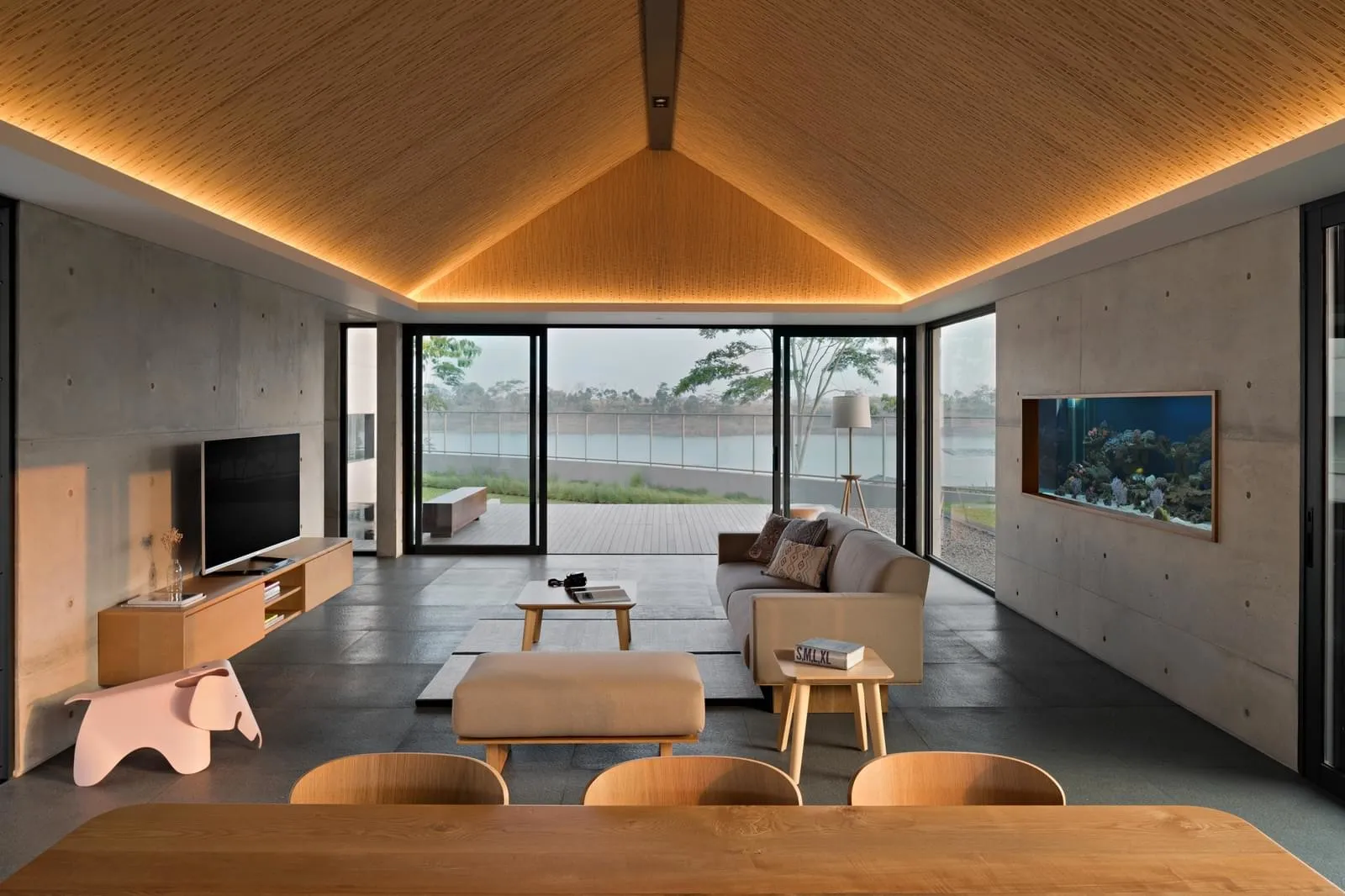 A modern living room with concrete walls, a wooden dining table, and a large aquarium.
