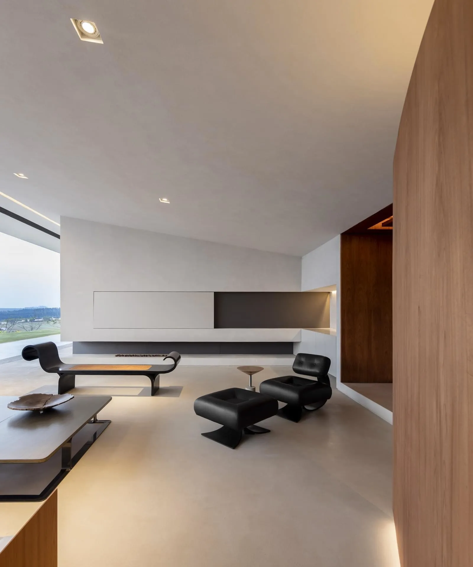 Modern living room with minimalist design featuring concrete walls, black furniture, and a large window.
