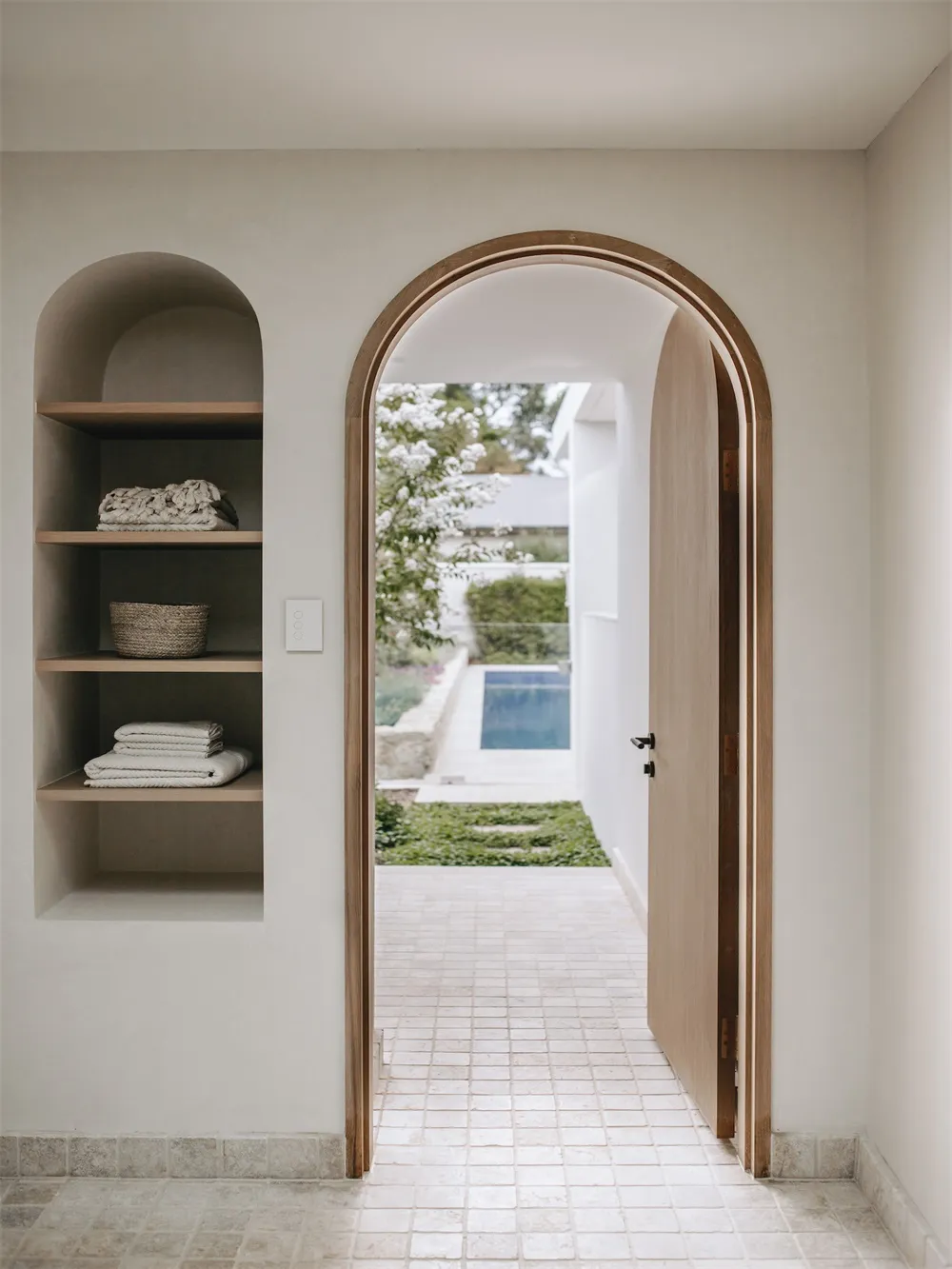 A minimalist residential exterior with an indoor-outdoor entrance featuring a wooden door.
