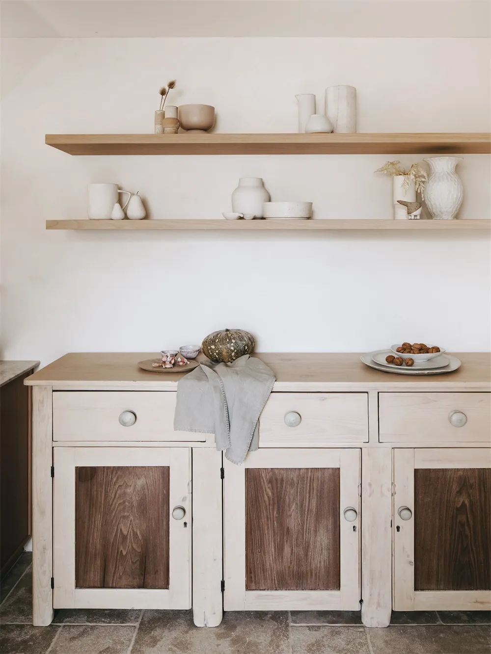 A minimalist kitchen with white cabinets and wooden accents, featuring decorative ceramics on shelves.