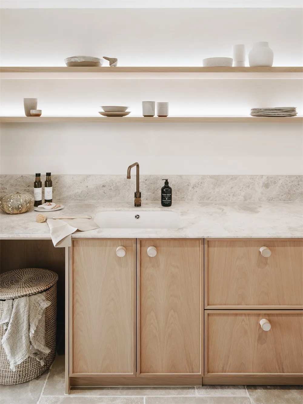 A modern minimalist kitchen with wooden cabinets, marble countertops, and a sink with a bronze faucet.
