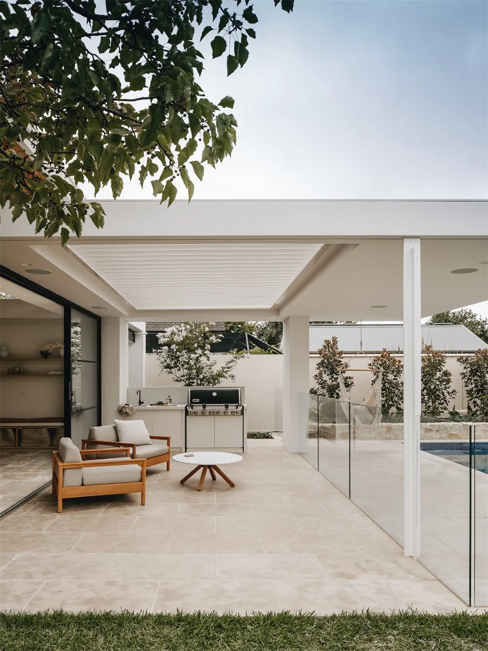 Modern outdoor kitchen and garden with tiled flooring and white outdoor furniture.