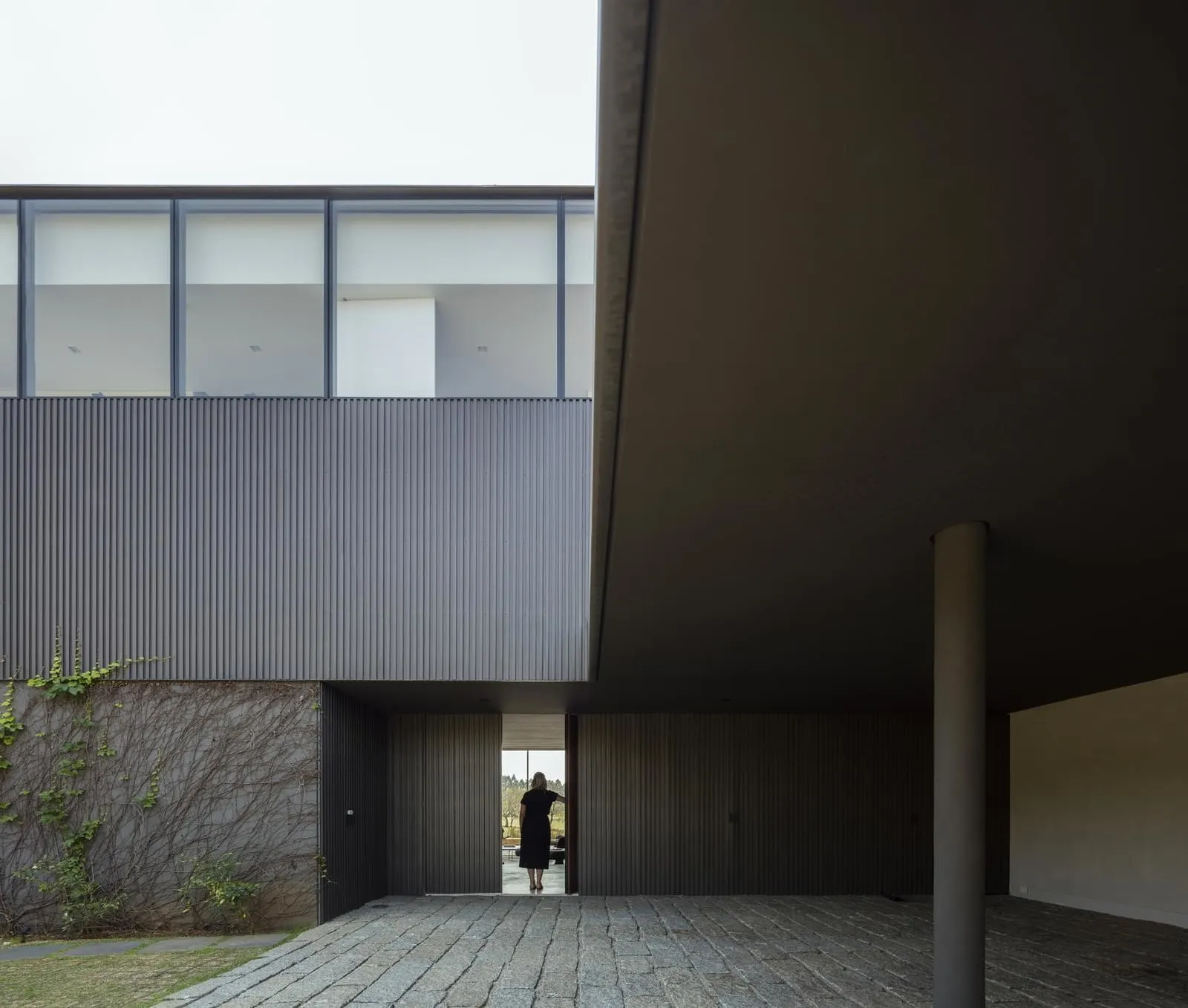 A modern residential exterior featuring metal-clad siding and a concrete floor.