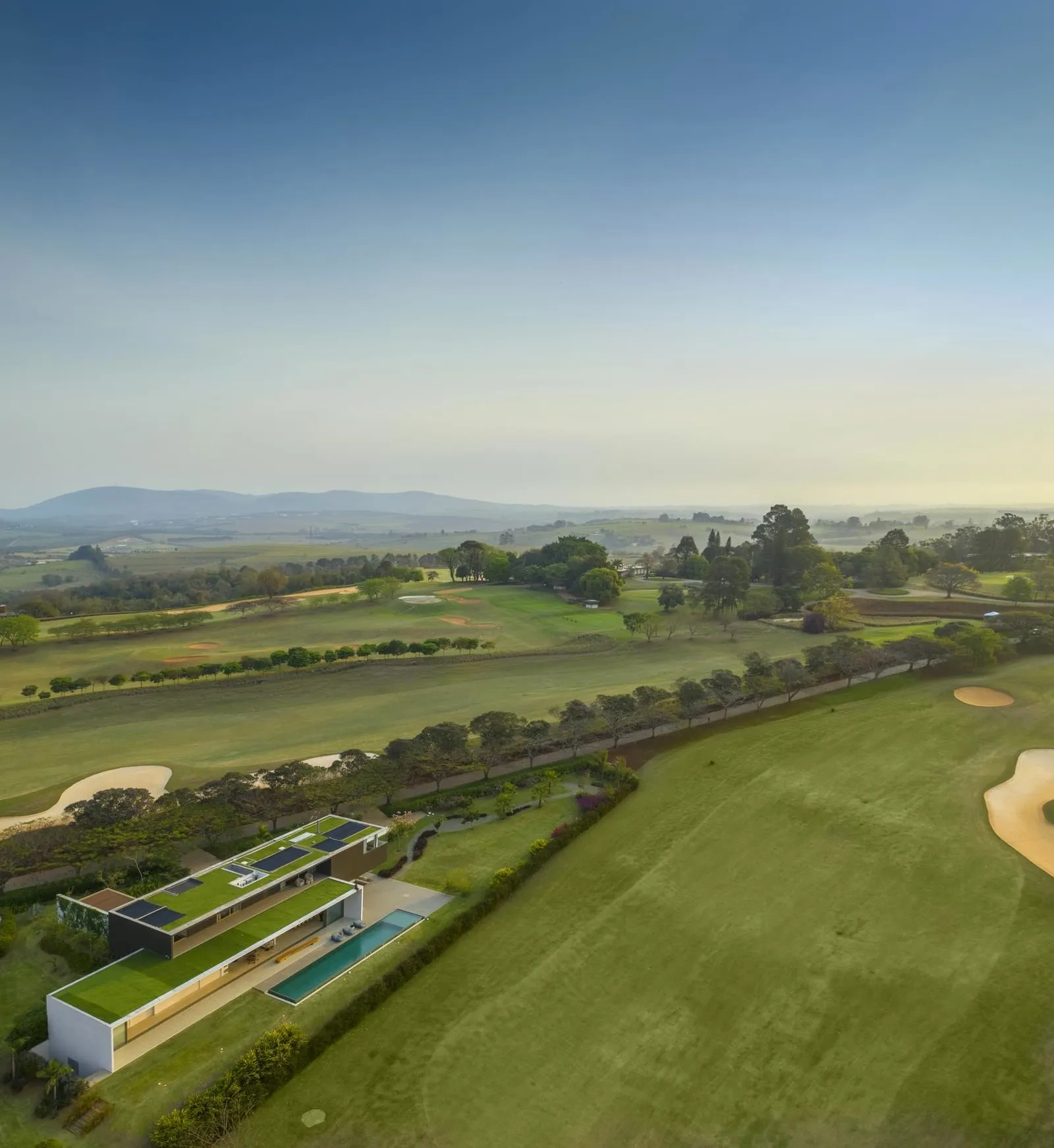 Modern residential home with a green roof and rooftop garden overlooking a golf course and countryside.