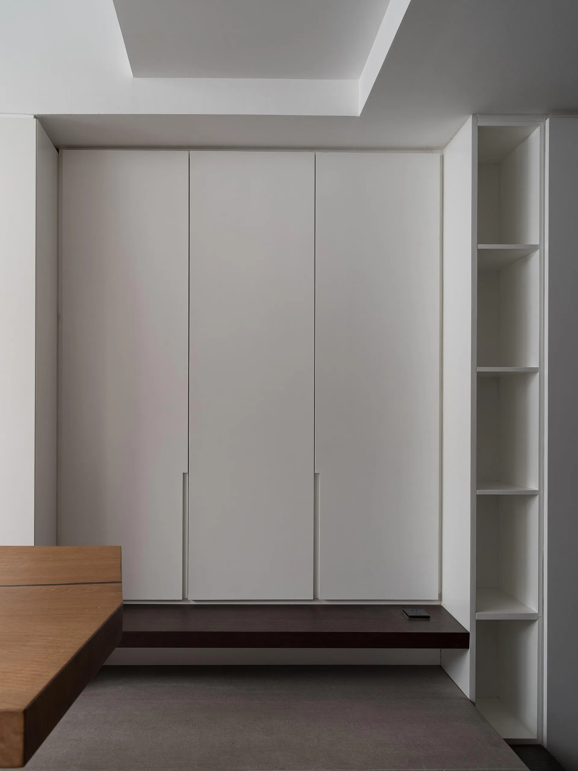 A minimalist bedroom featuring white cabinets and wooden furniture.