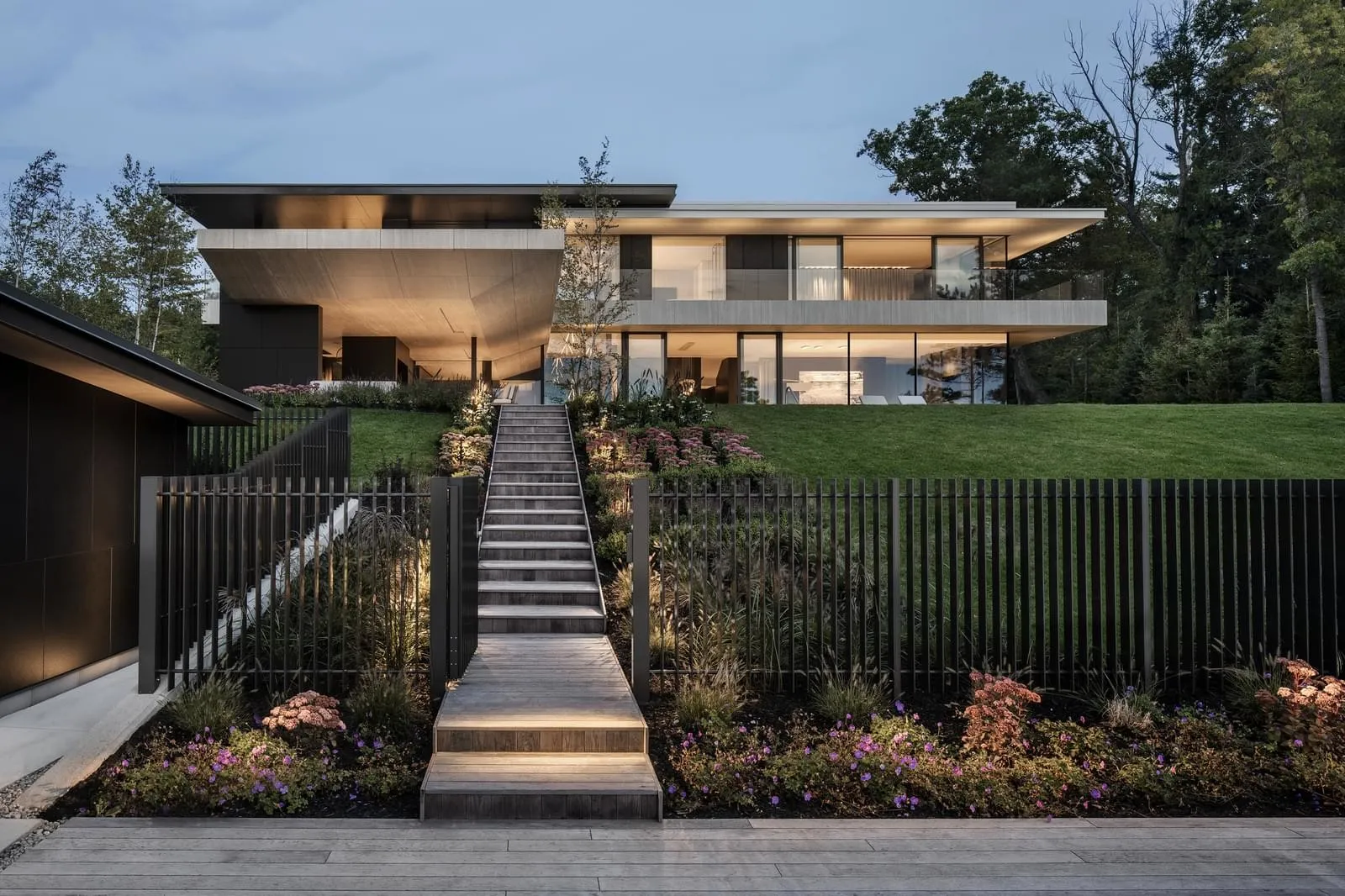 A modern, two-story house with large windows and a wooden staircase leading up to it.