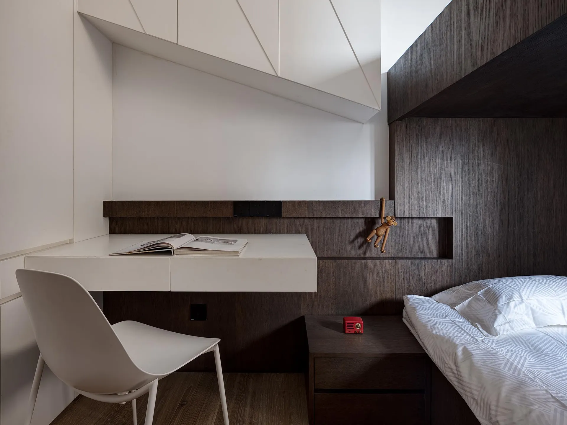 Modern bedroom with minimalist design, featuring a white chair and a bed with a white and gray patterned duvet.