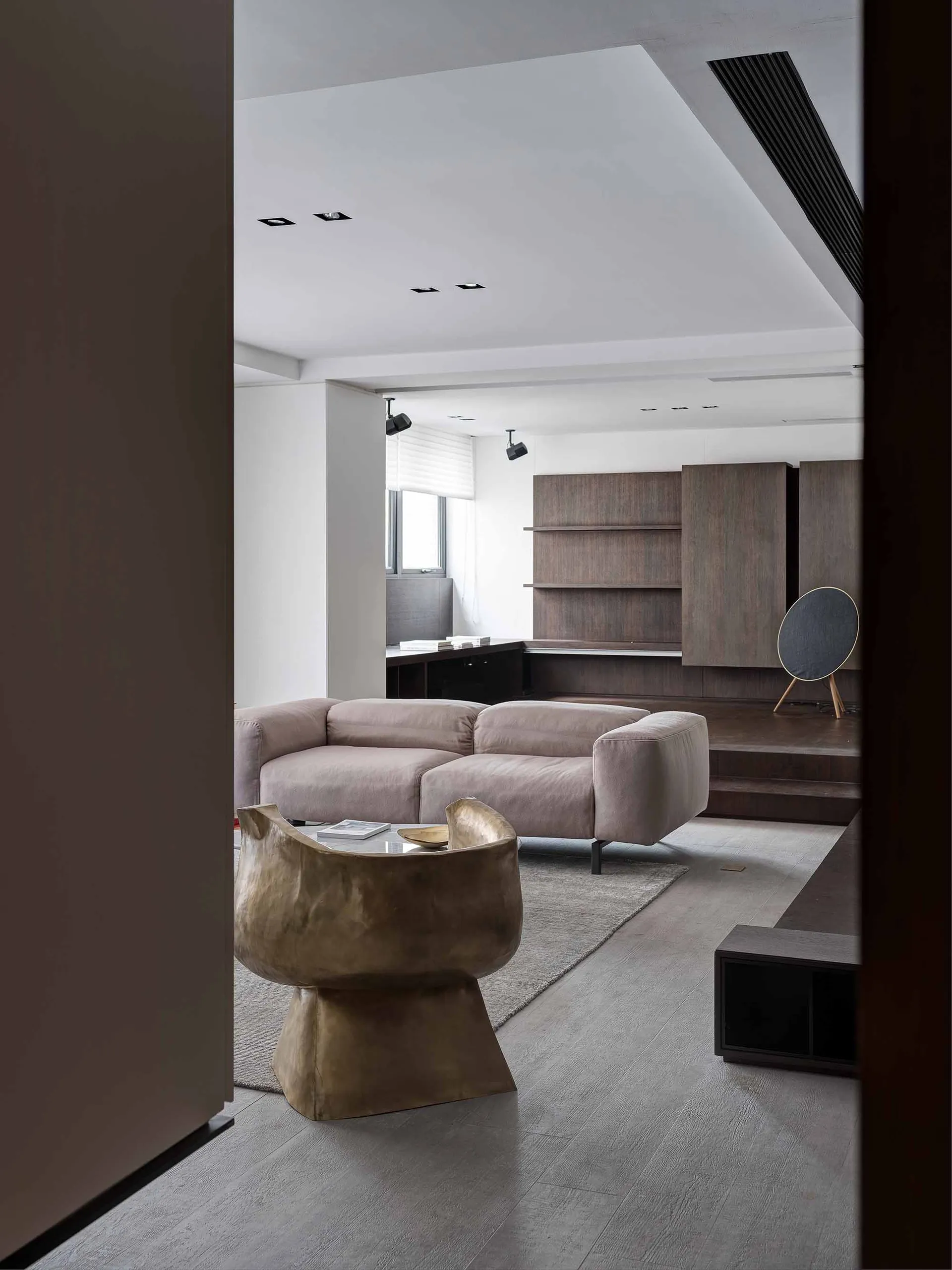Modern living room with minimalist design featuring a beige sofa, wooden shelves, and a unique metallic side table.