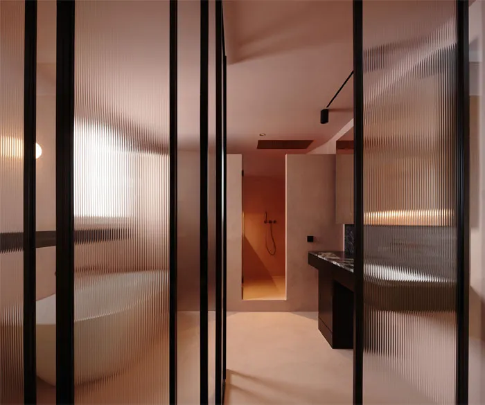 A minimalist bathroom with a glass partition, white bathtub, and black accents.
