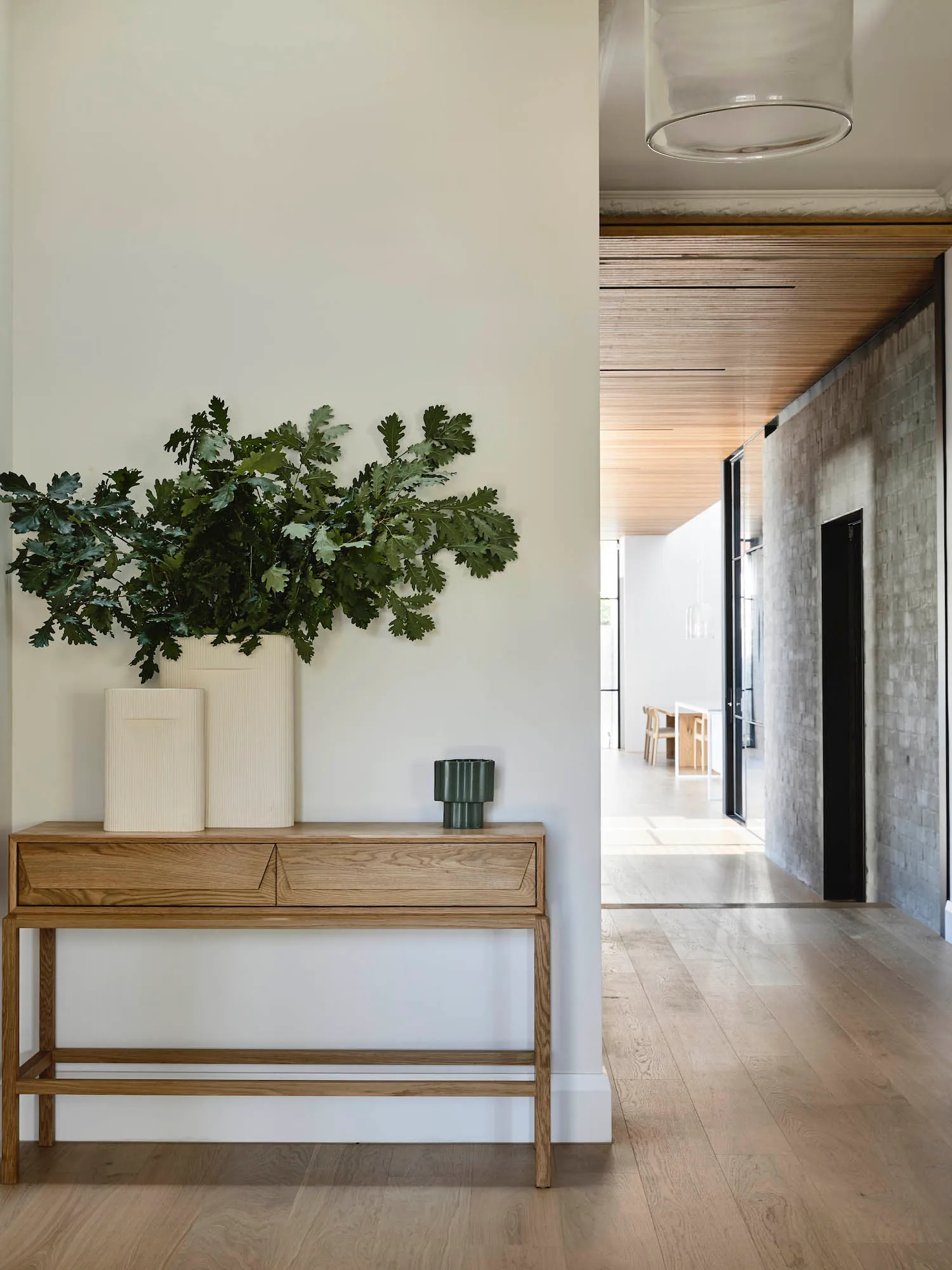 A minimalist interior design featuring a wood console table with a vase and plants, set against a white wall and wooden floor