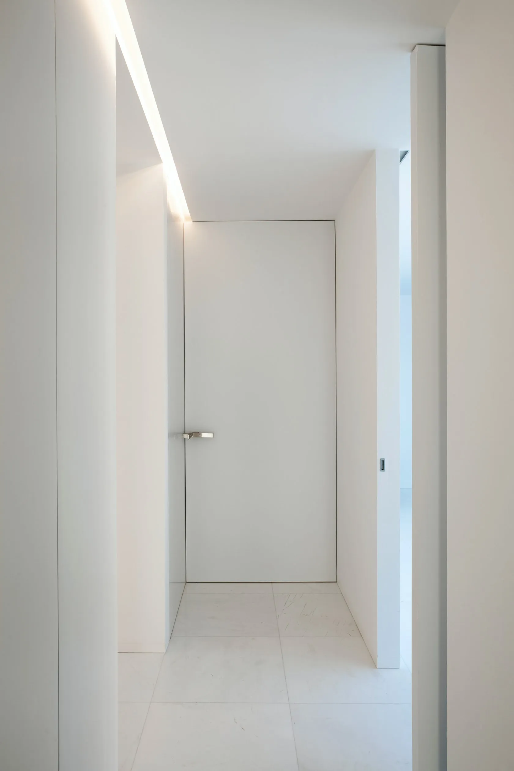 A minimalist doorway with a white door against a concrete wall, illuminated by soft lighting.