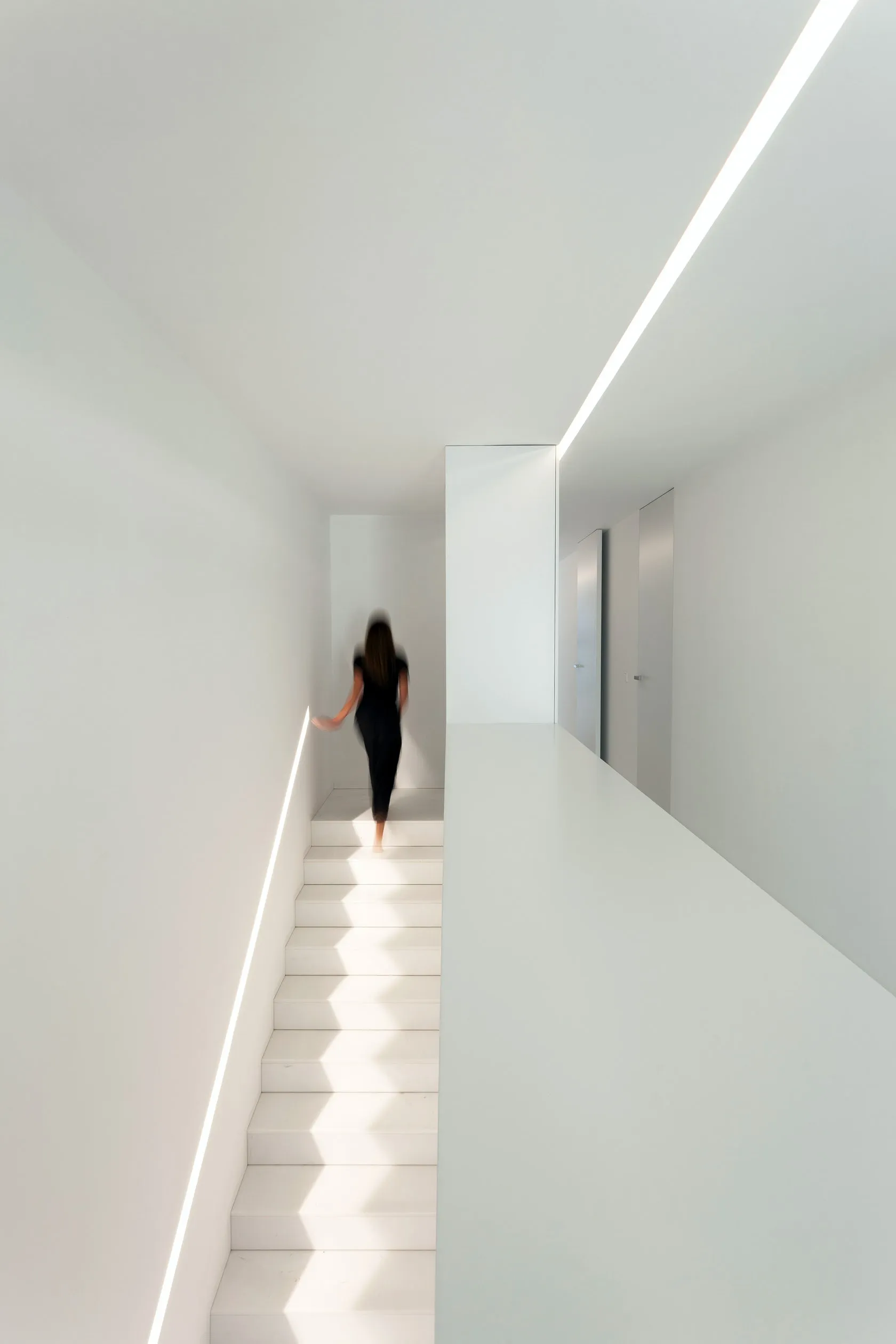 A minimalist staircase with white steps and walls, featuring a single person ascending from the background.