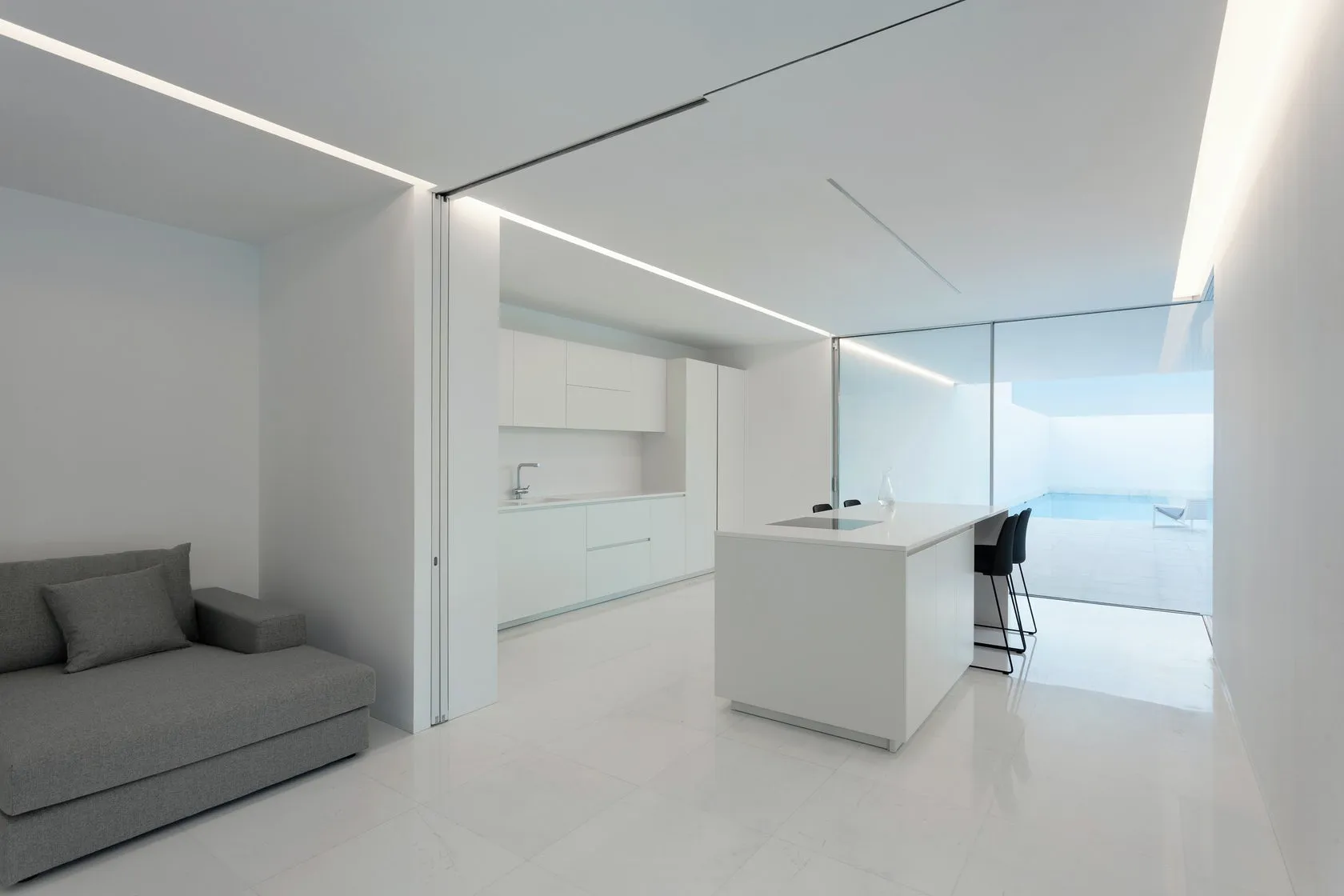 Empty room with modern minimalist design, featuring white walls and floor, minimalist furniture, and a kitchen with a white i