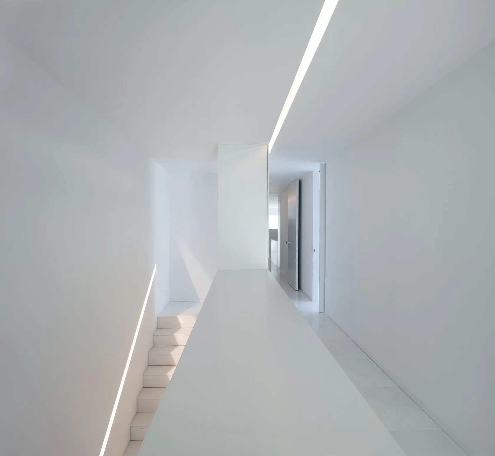 A minimalist white interior with a white wall and floor, featuring a staircase with white steps and a light source from above