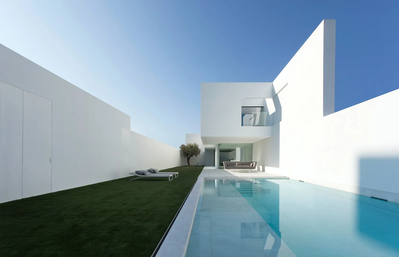 Modern minimalist house exterior with white marble pool and garden.