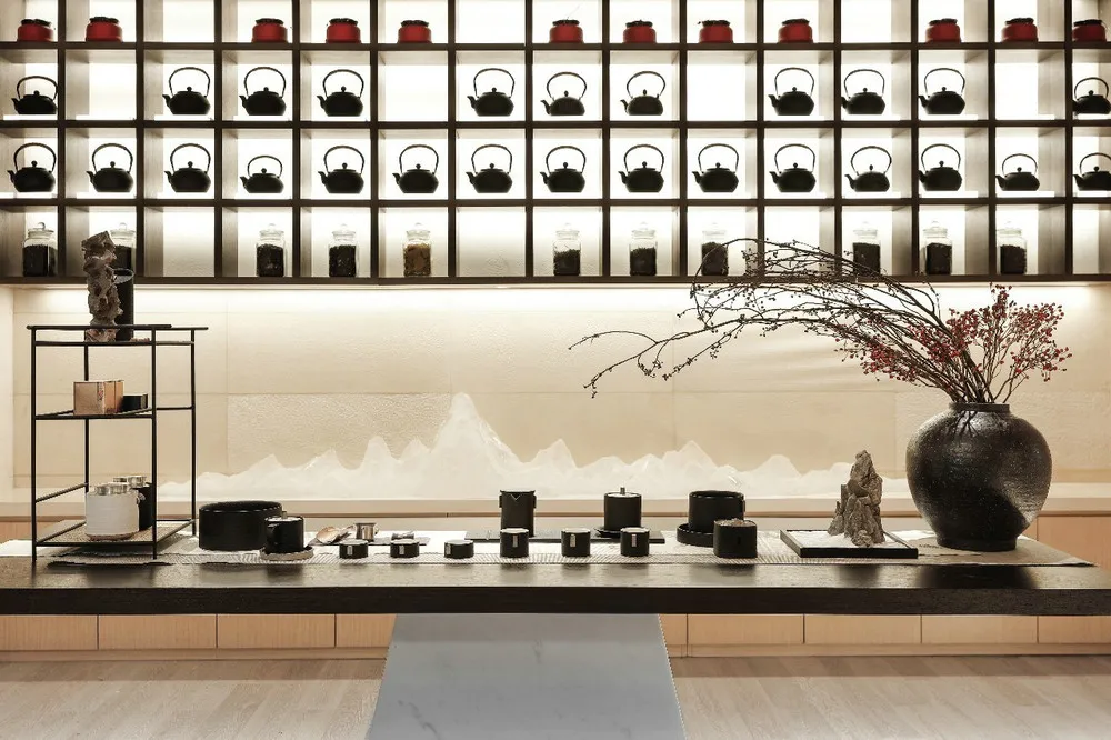A modern tea room features a wall display of ceramic teapots and vases arranged in a grid pattern, enhancing the aesthetic an