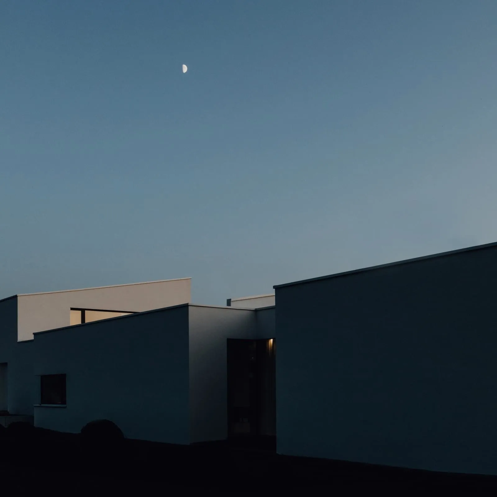 極簡風格的現代建築外觀，夜空懸掛一彎新月。