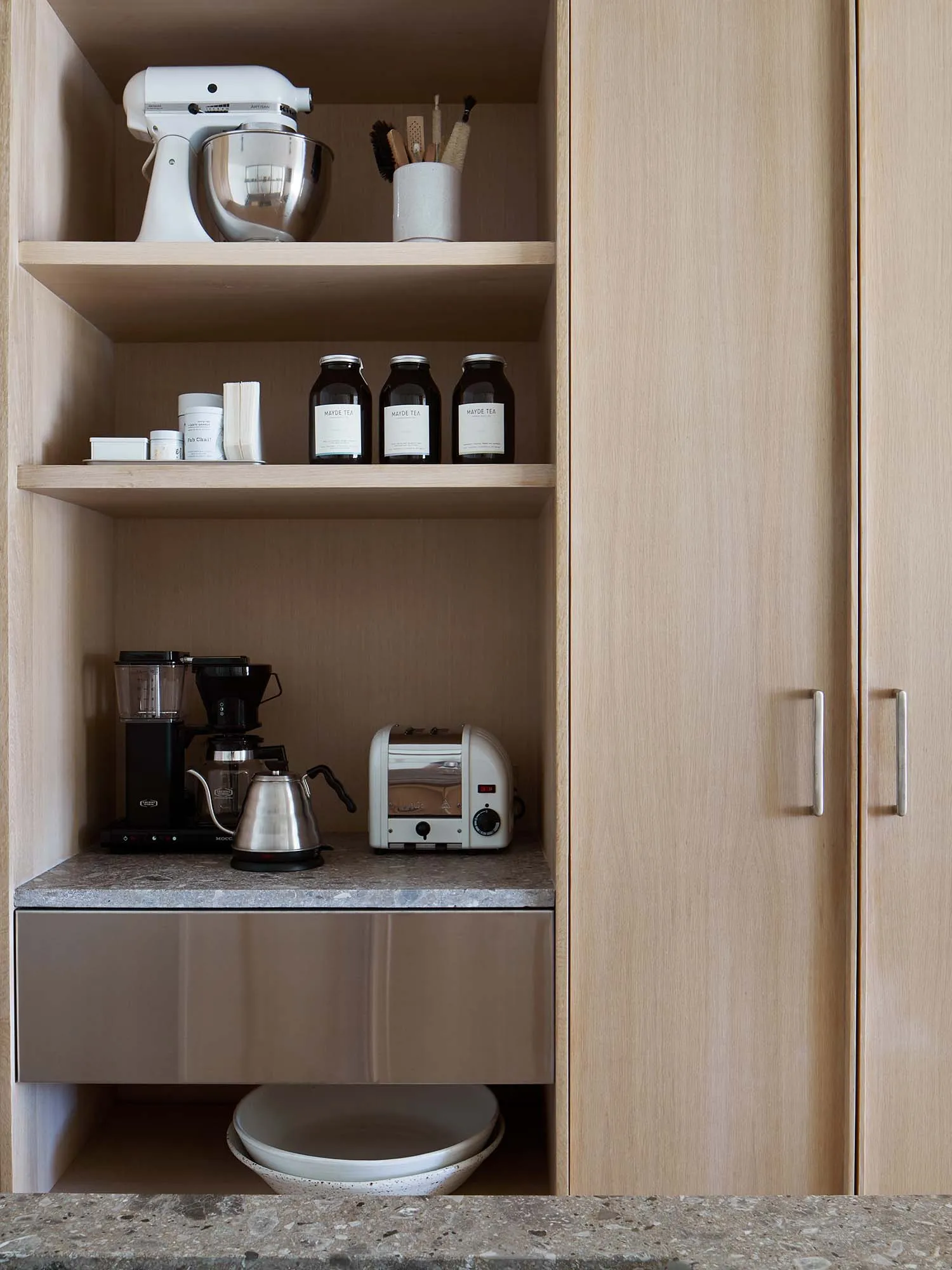 A modern minimalist kitchen with wooden cabinets and a grey countertop, featuring essential appliances like a toaster, kettle