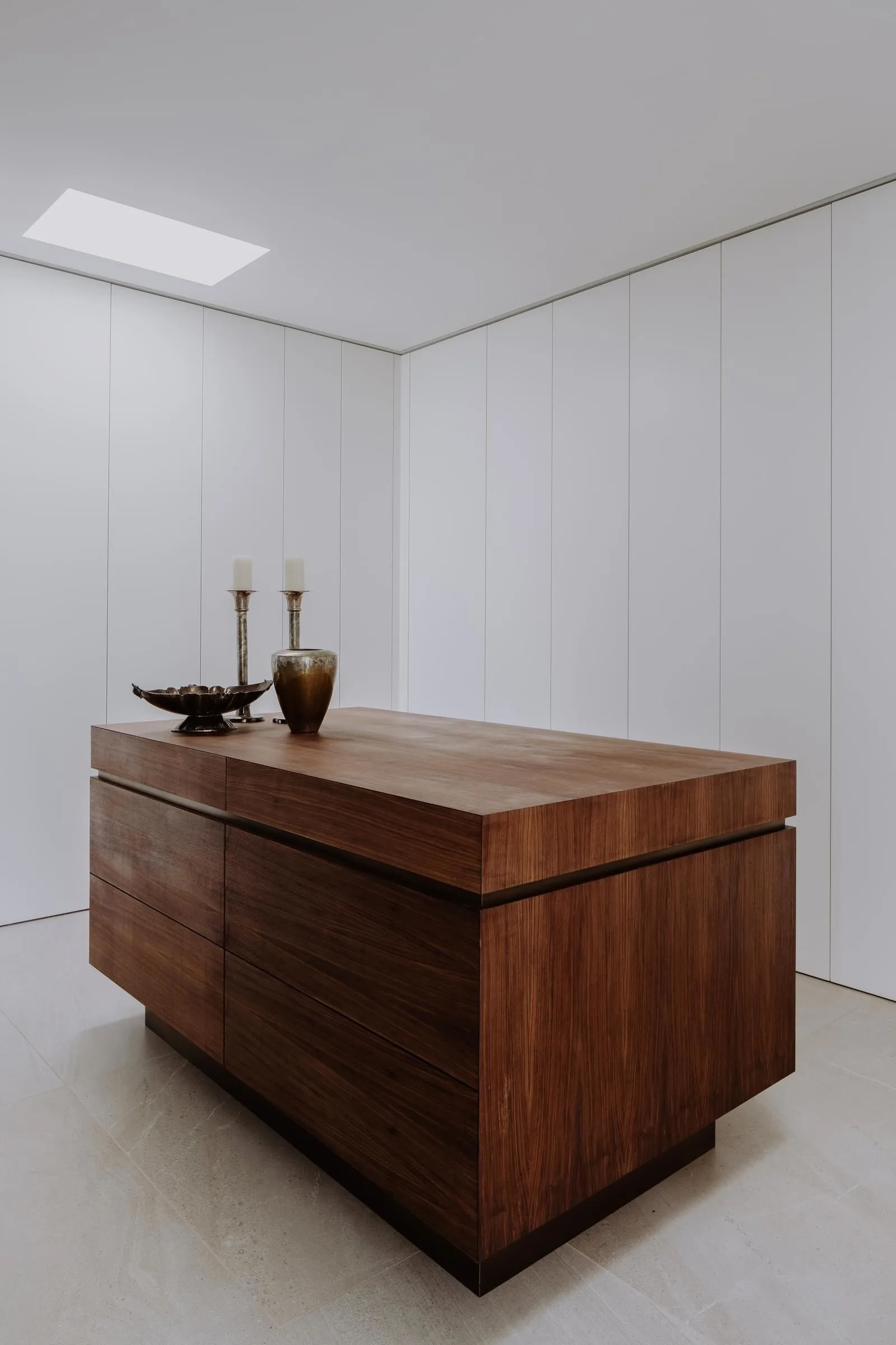 A modern, minimalist bedroom featuring an elegant wooden dresser and white walls.