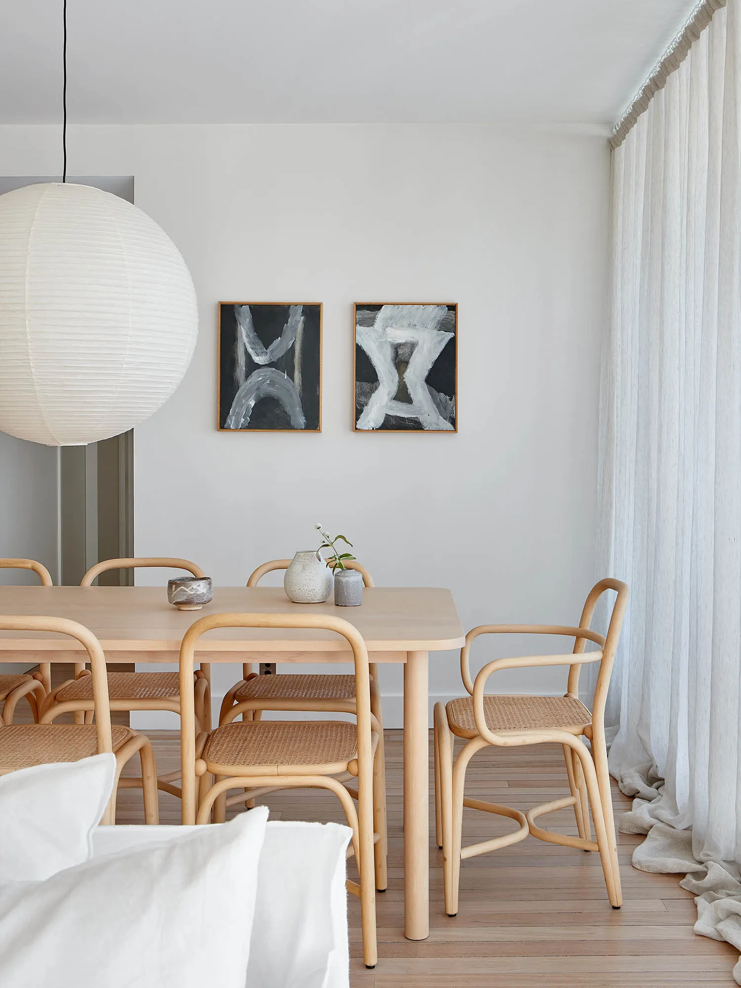 A modern minimalist dining room featuring wooden furniture and light-colored woven chairs.