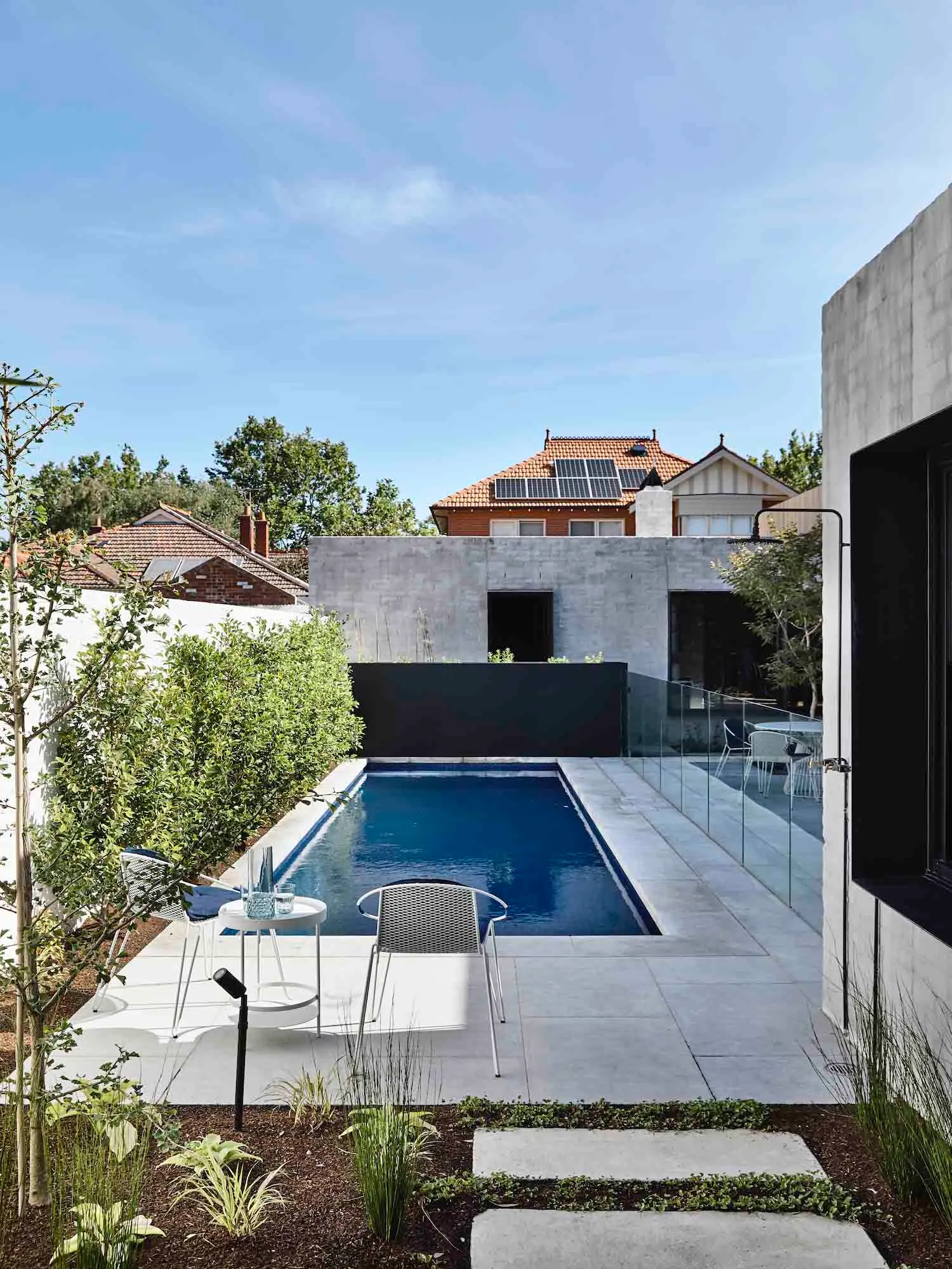 A modern pool deck featuring a rectangular swimming pool bordered by concrete tiles, with a minimalist aesthetic and surround