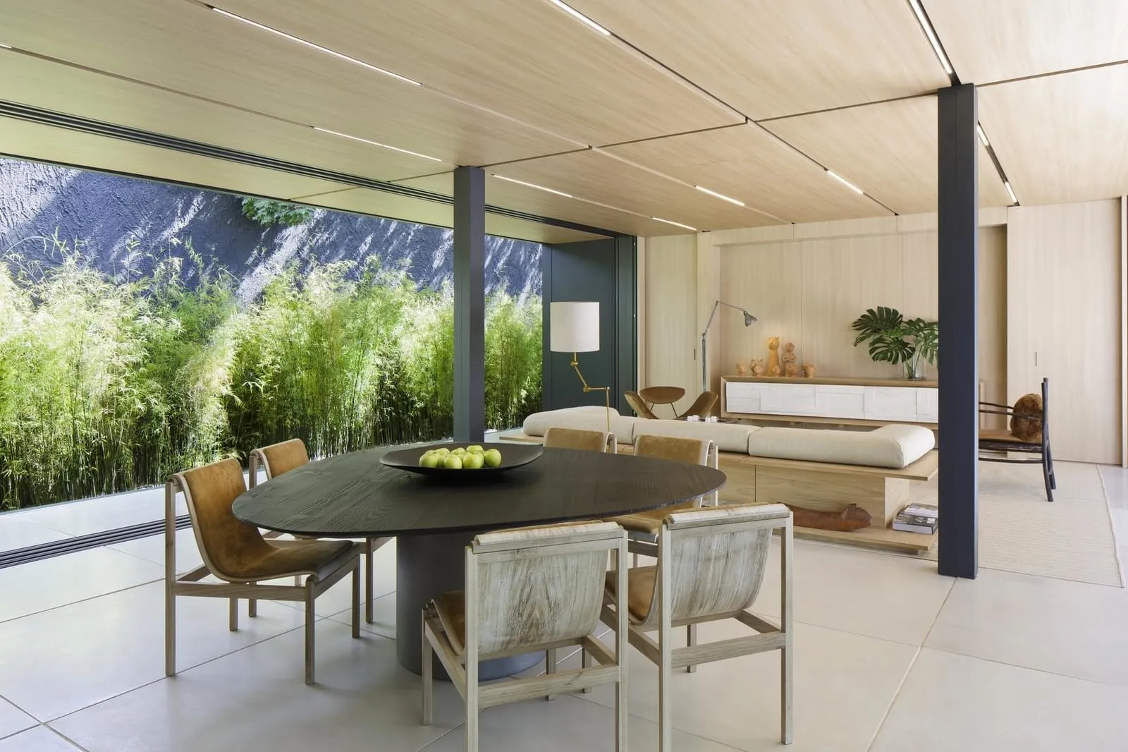 A minimalist living space with a wooden dining table and chairs, surrounded by lush greenery and natural light.