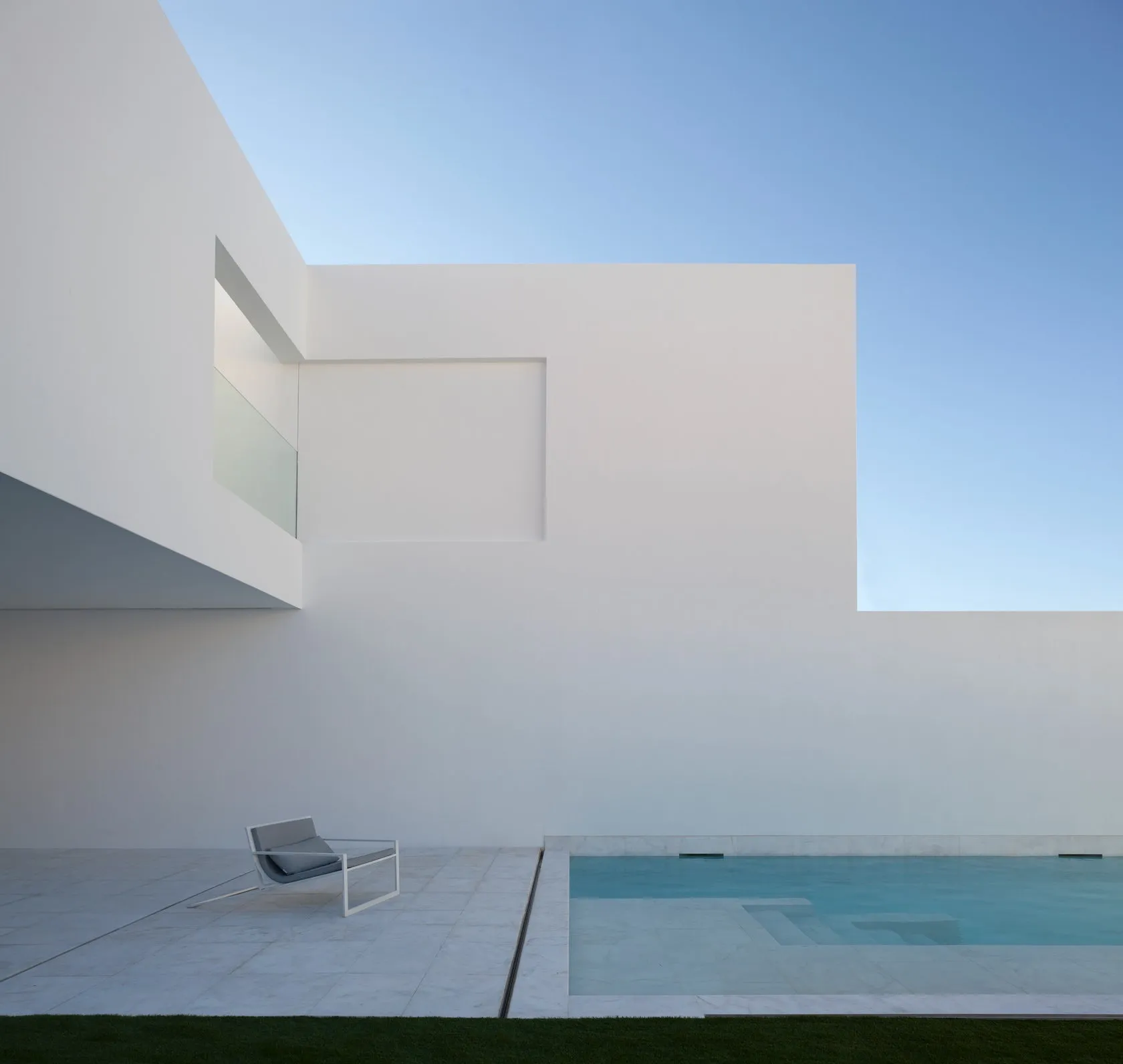 Modern minimalist house with white walls, glass window, and concrete patio and pool.