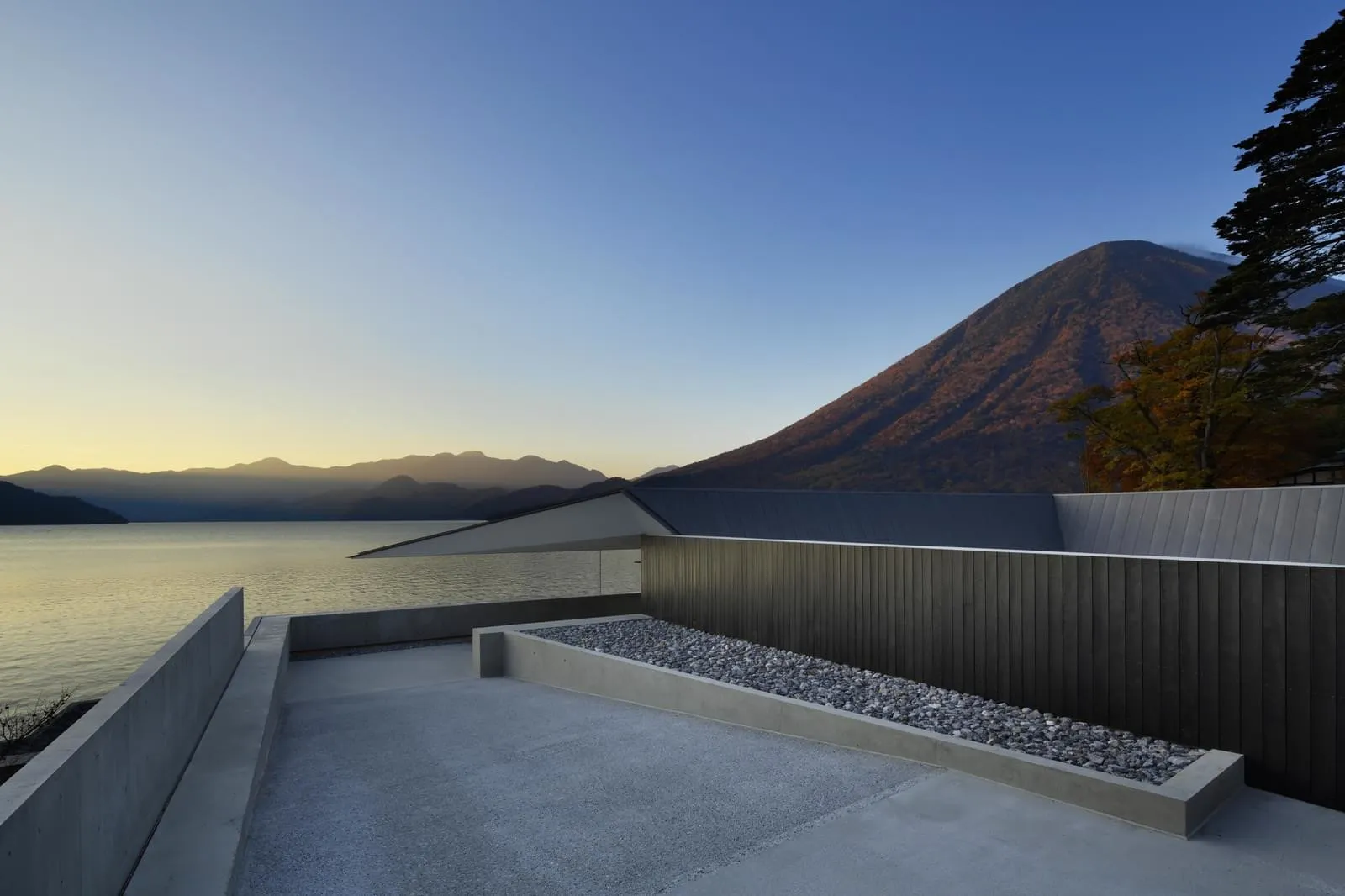 一座現代混凝土住宅,擁有可俯瞰湖泊與山景的屋頂露台。