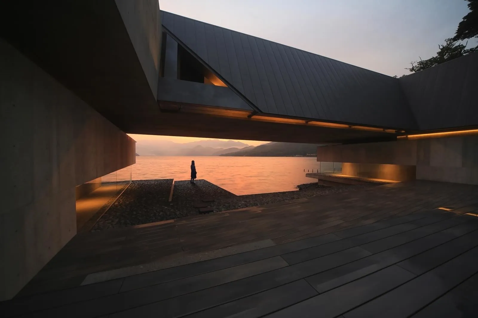 A modern, concrete and wooden cabin by the lake at sunset