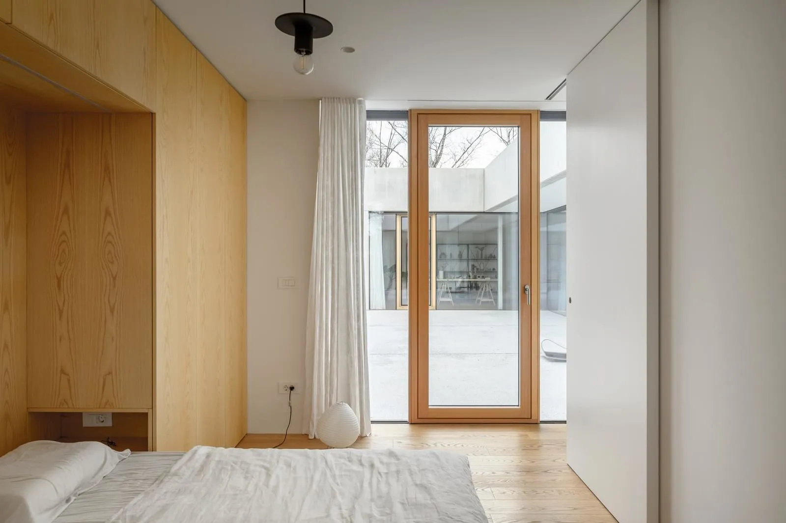 A minimalist bedroom with wooden furniture and a glass door.