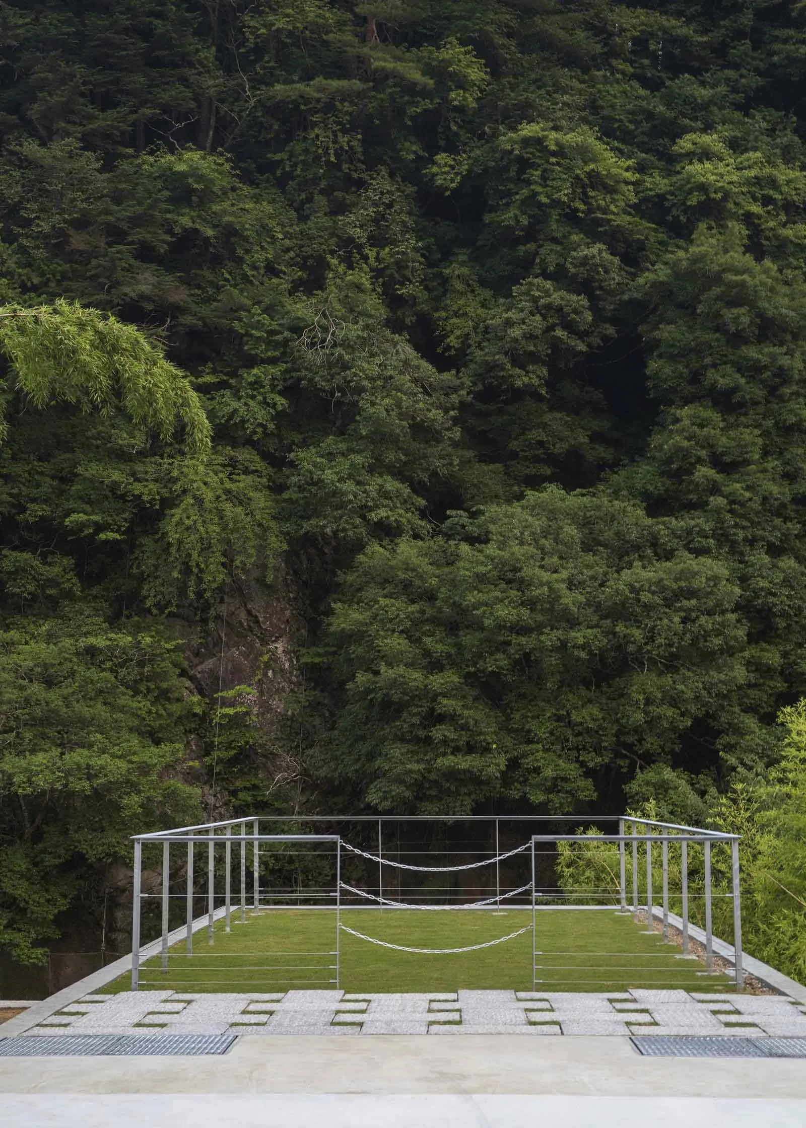 Minimalist architectural structure with metal frame and concrete platform surrounded by lush greenery in a forest setting.