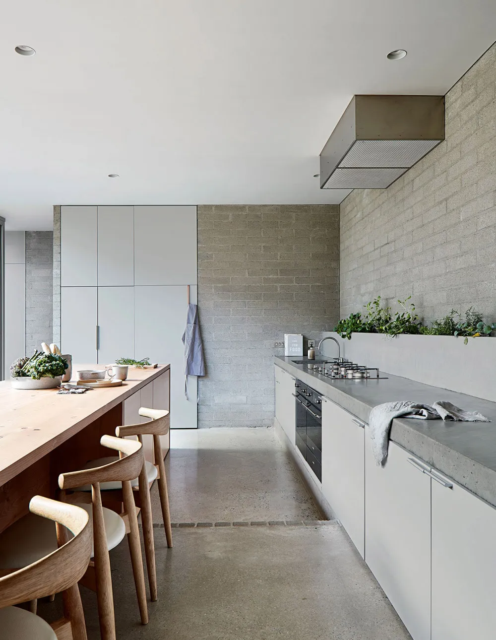 Modern minimalist residential kitchen with concrete countertops and white cabinets.