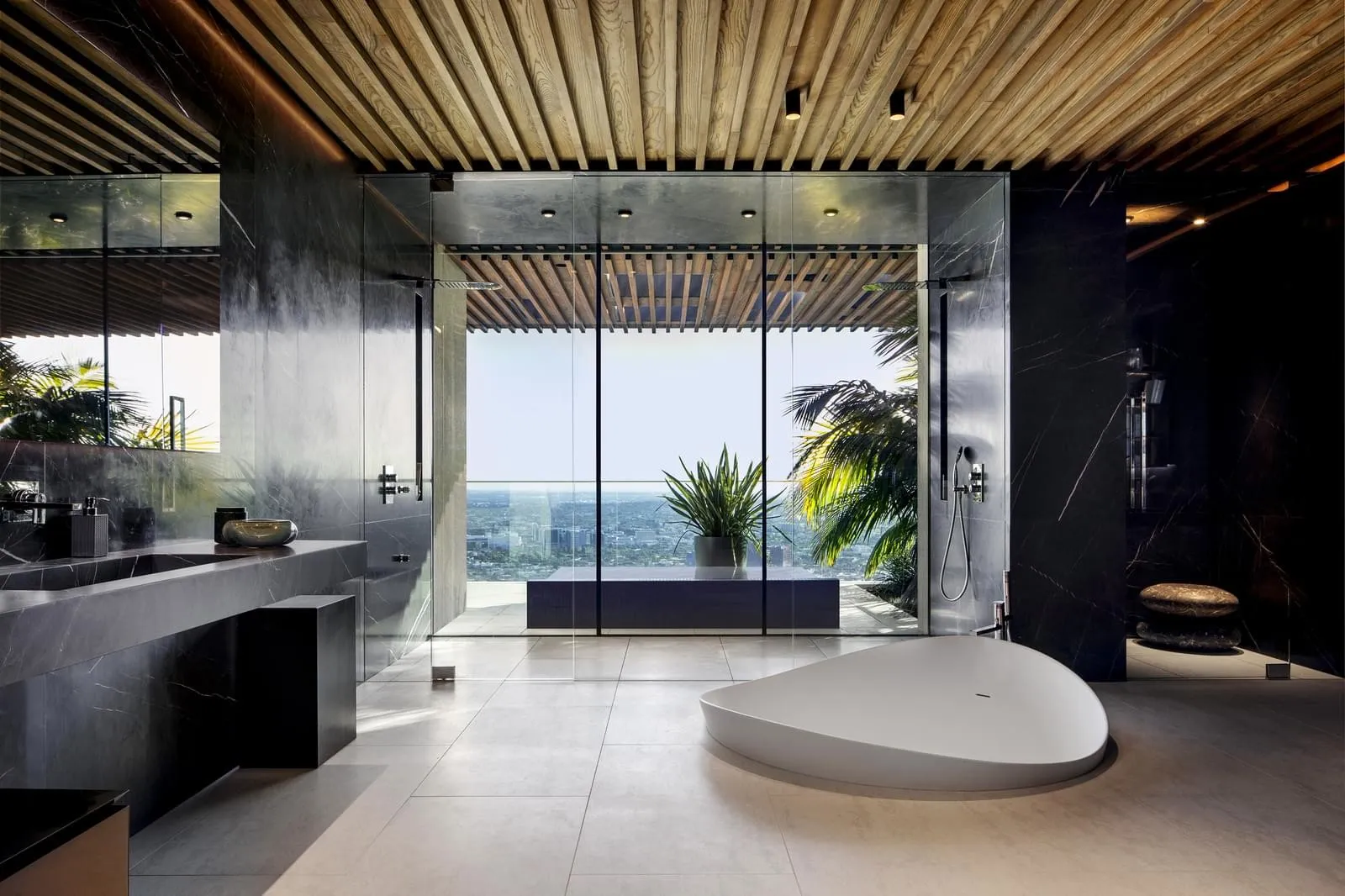 A modern bathroom with large glass windows showcasing an urban view, featuring sleek black marble accents and a large freesta