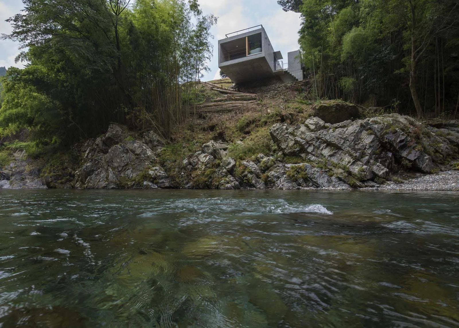 A modern concrete house built on a steep hillside overlooking a river.