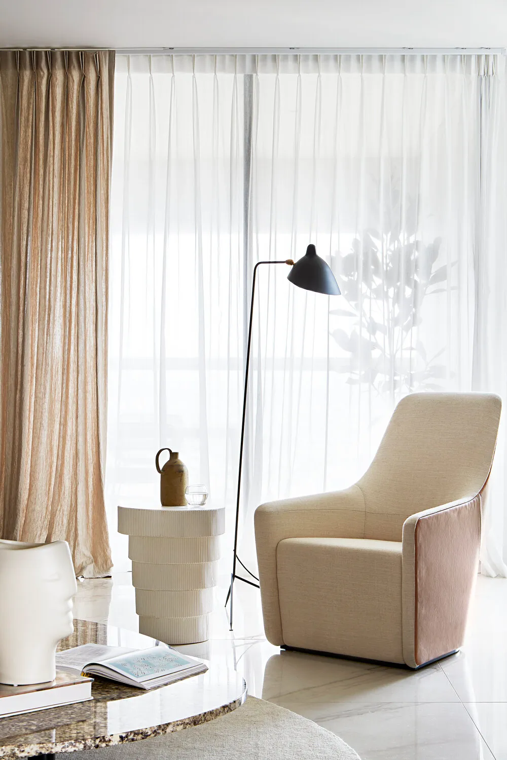 現代客廳內有白色紋理窗簾、燈具,以及靠近窗邊的 upholstered 椅。
