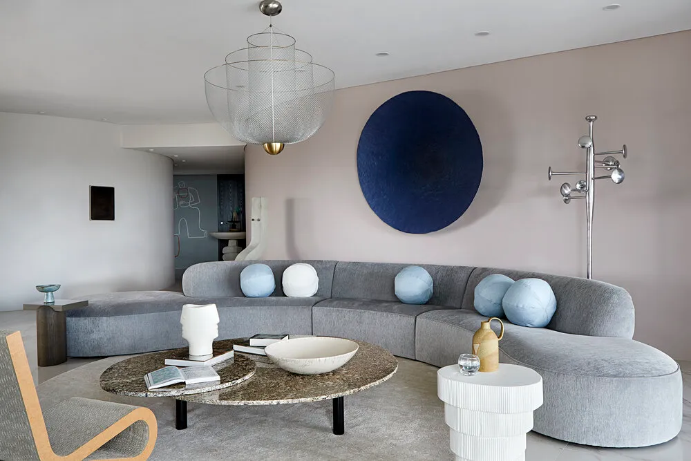 A modern living room featuring a curved gray sofa, marble side tables, and metal floor lamp.