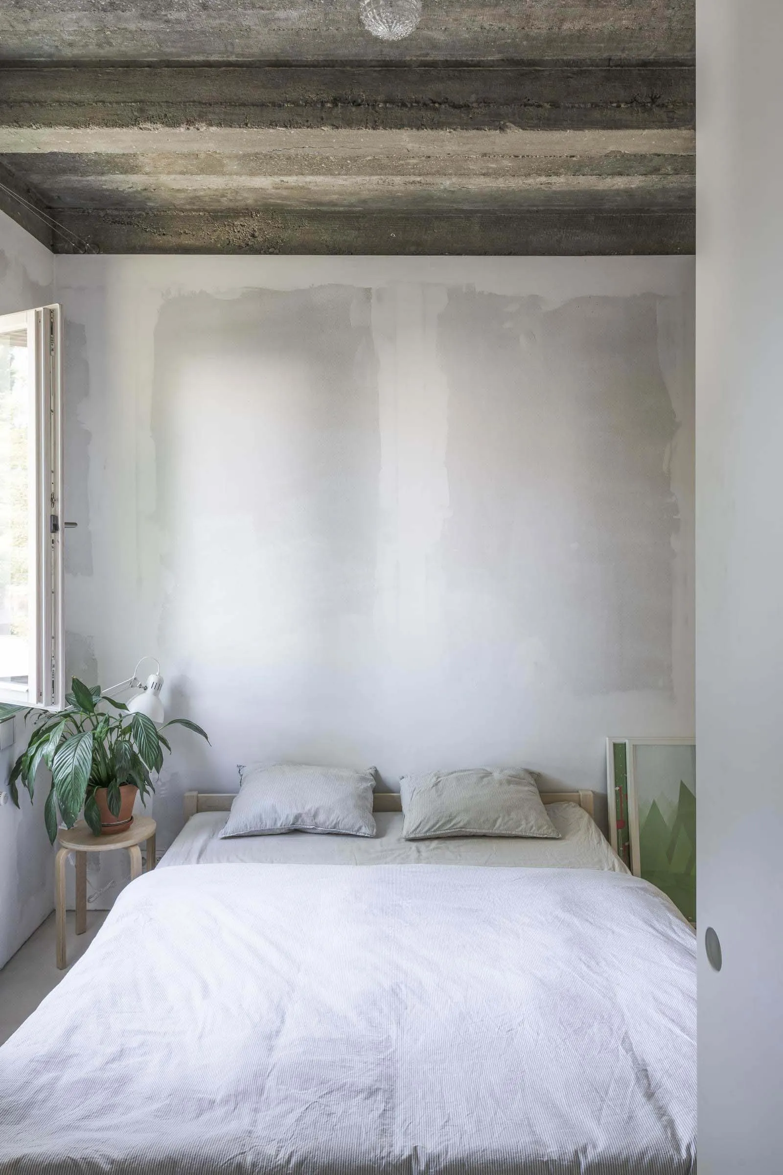 Sparse bedroom with concrete ceiling, white bedding, and minimalist design.