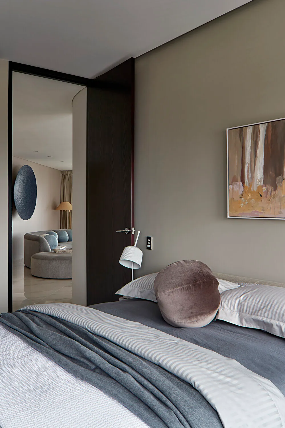 A minimalist bedroom with grey and taupe tones, featuring a bed, pillows, and a painting.