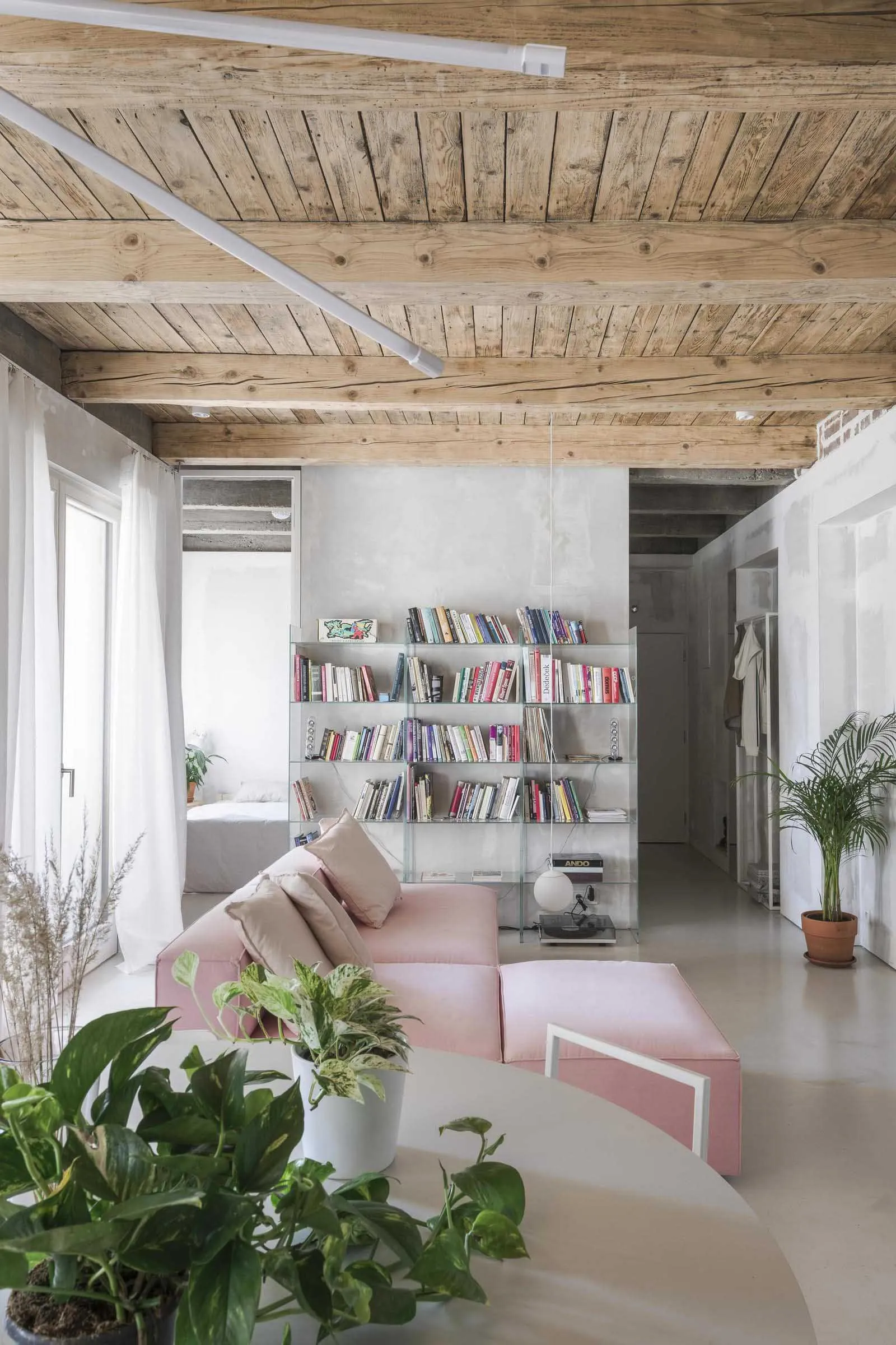 Minimalist living room with glass shelves, concrete flooring, and pink upholstered furniture.